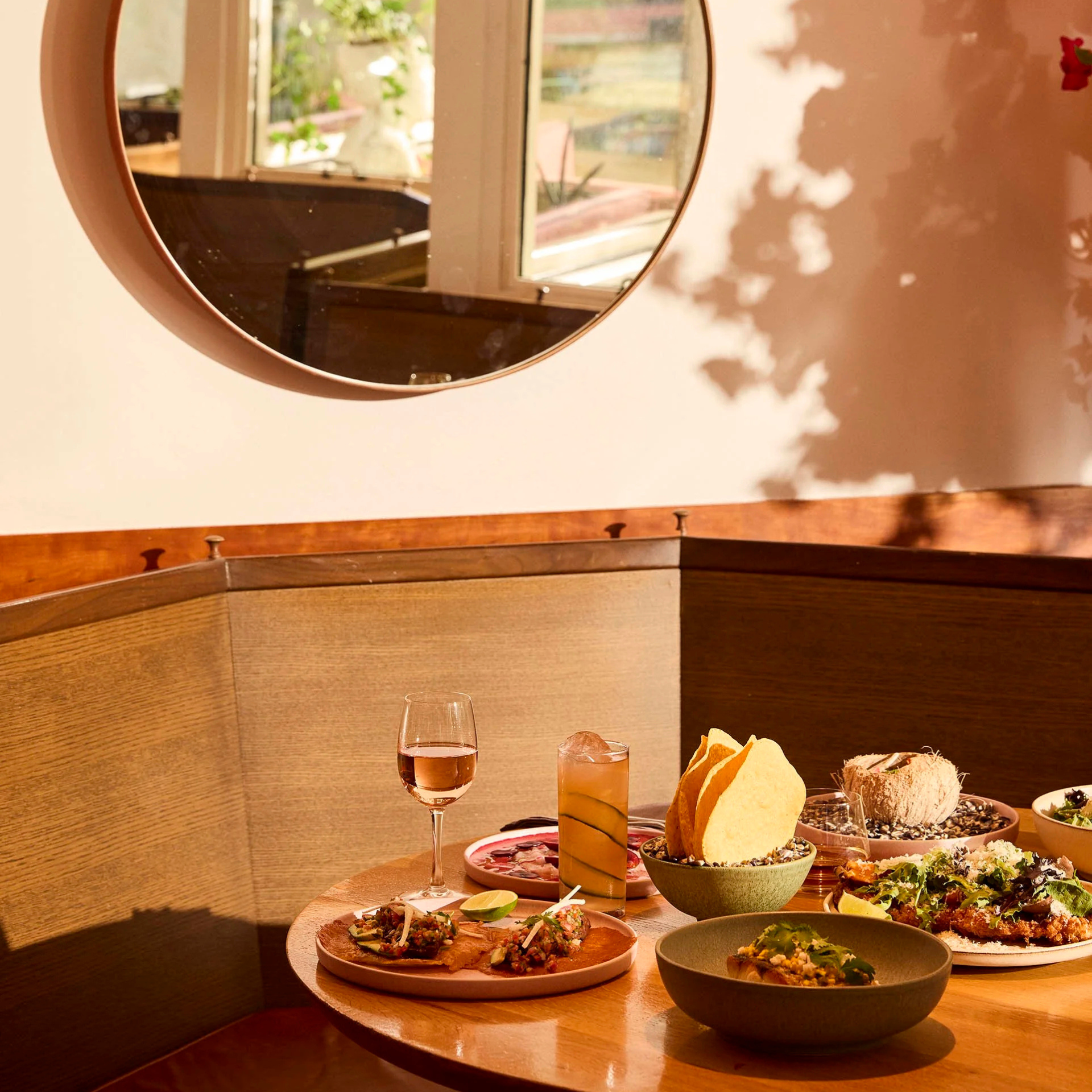 Corner booth with a round table set with tacos, salad, chips, and drinks in a warmly lit restaurant