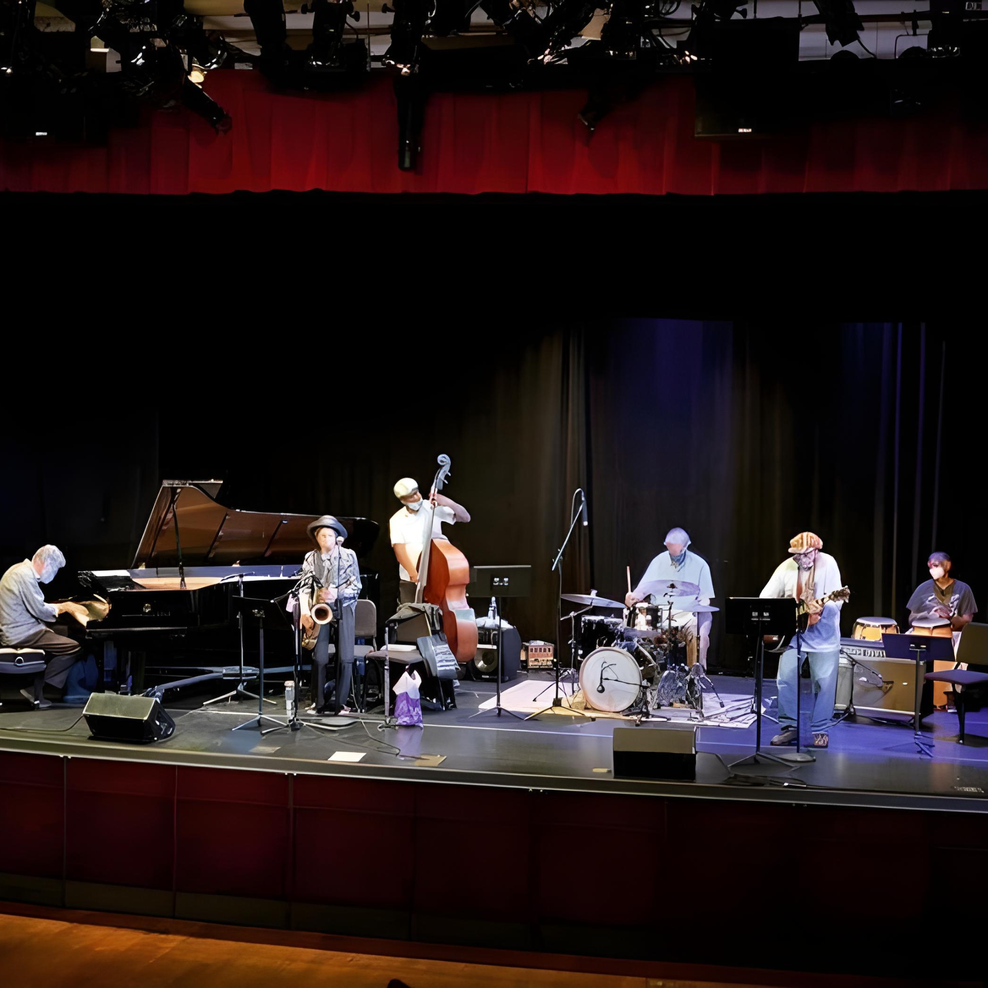 Live jazz band on stage with six musicians playing piano, saxophone, bass, drums, and guitars