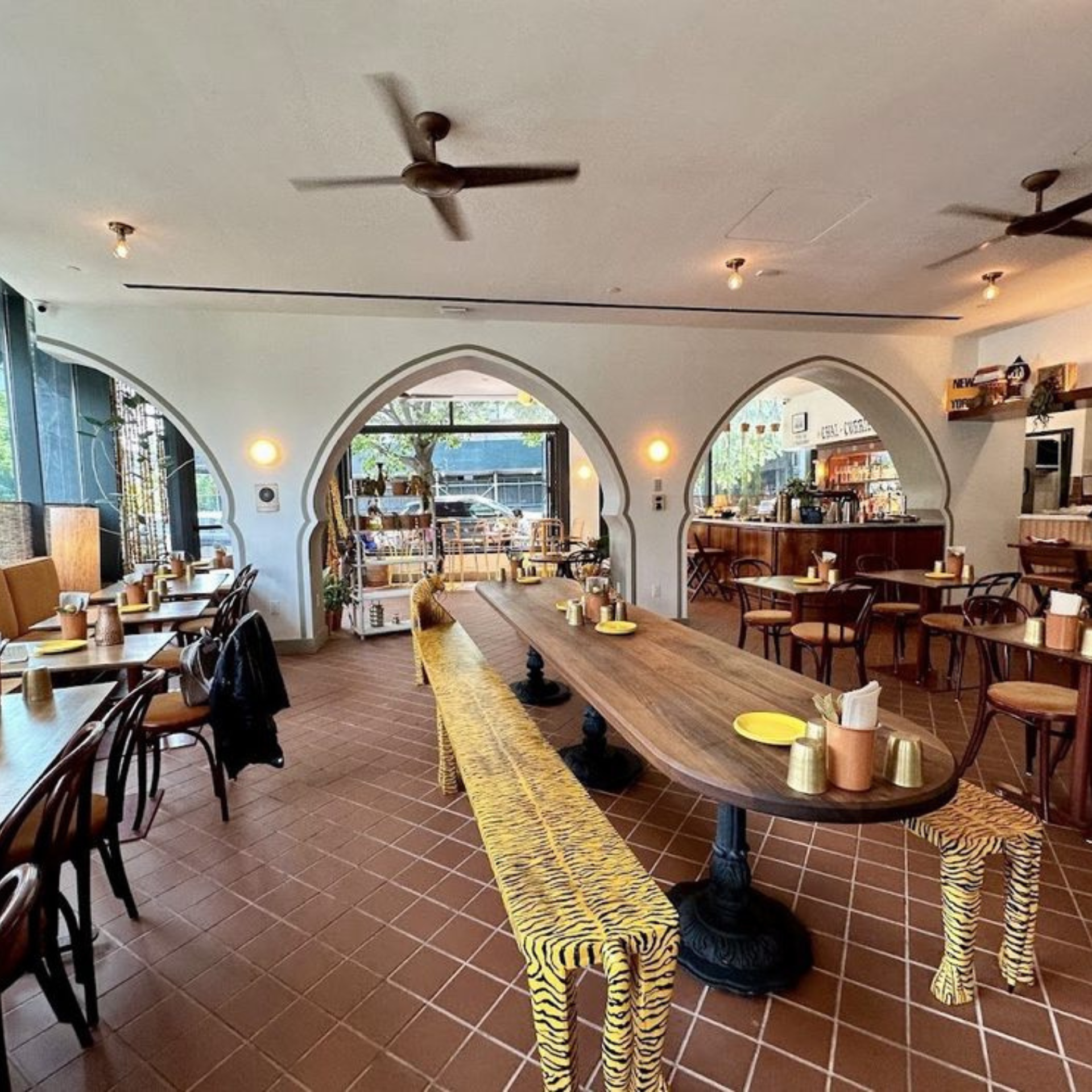 Warm café interior with terracotta tiles, communal tables, and bold yellow tiger-stripe benches
