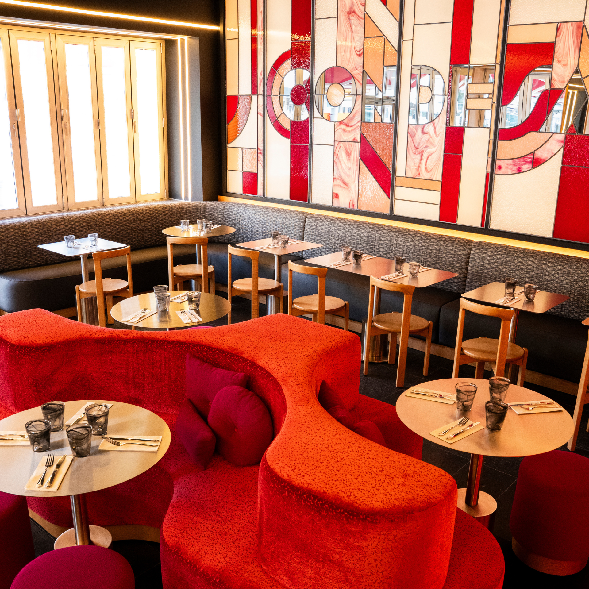 Modern café interior with red curved bench, abstract mural, and sunlit wooden tables