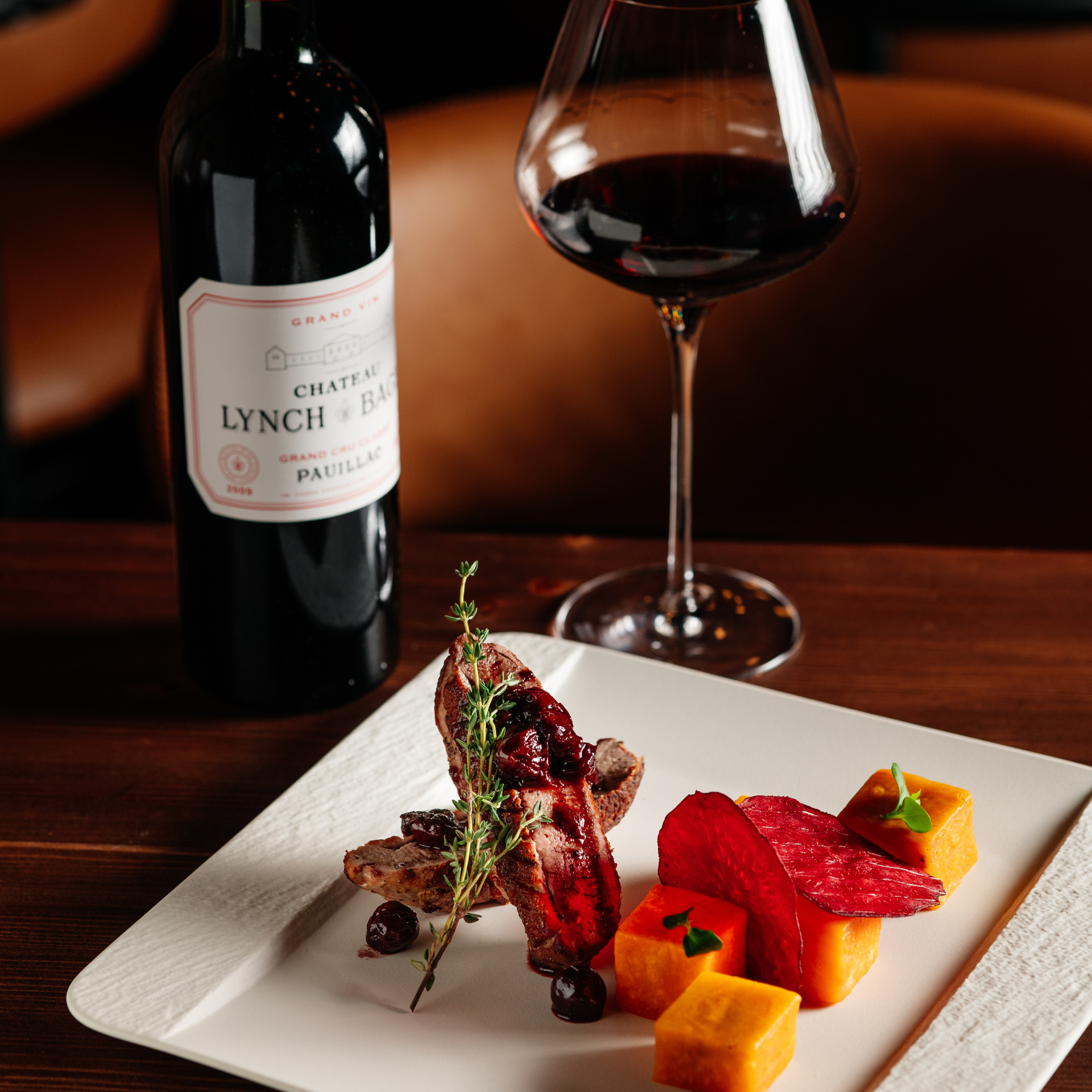 Gourmet dish with seared meat, vegetables, and red wine served on a white plate