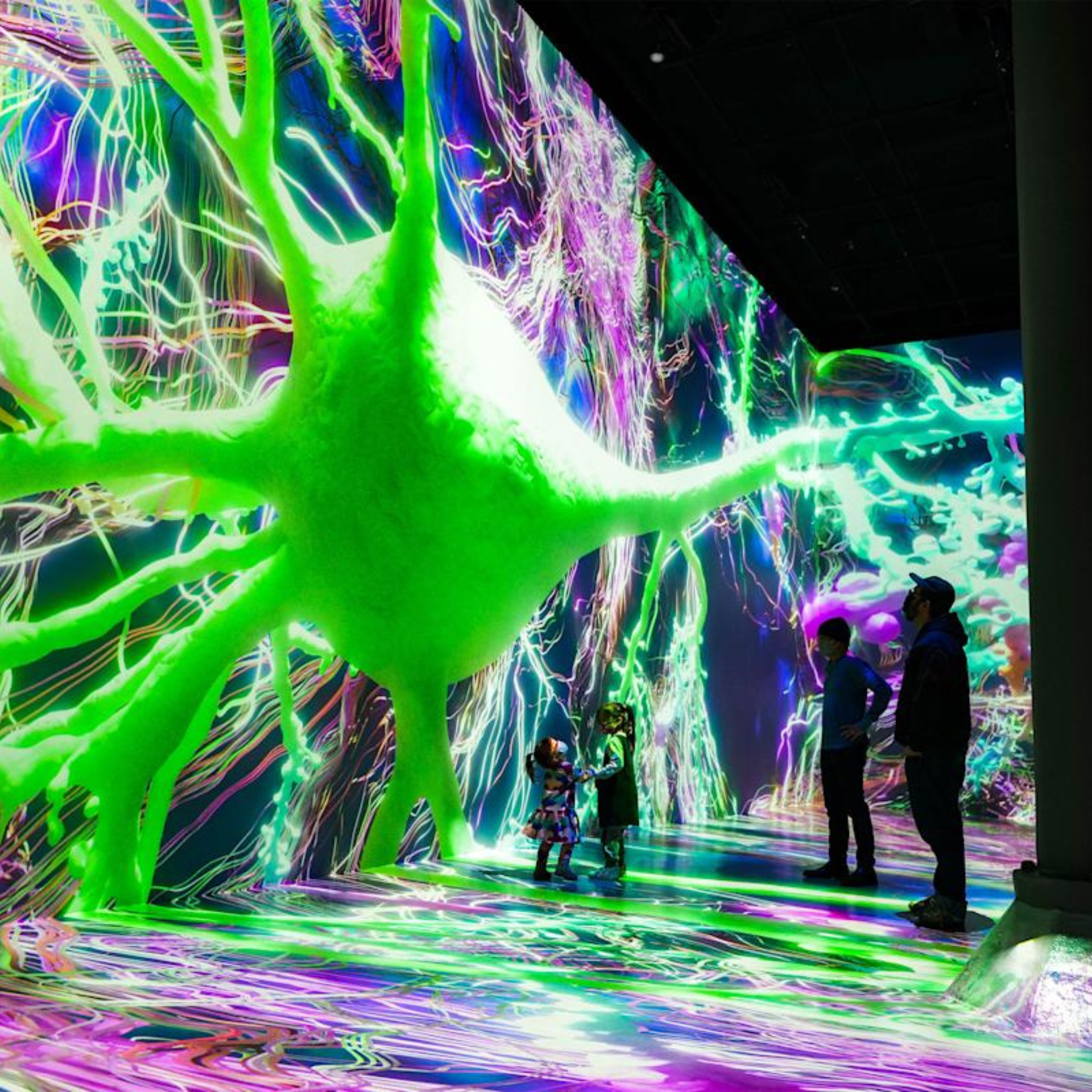 Visitors explore a glowing, neuron-themed digital art installation with vivid colors and branching patterns