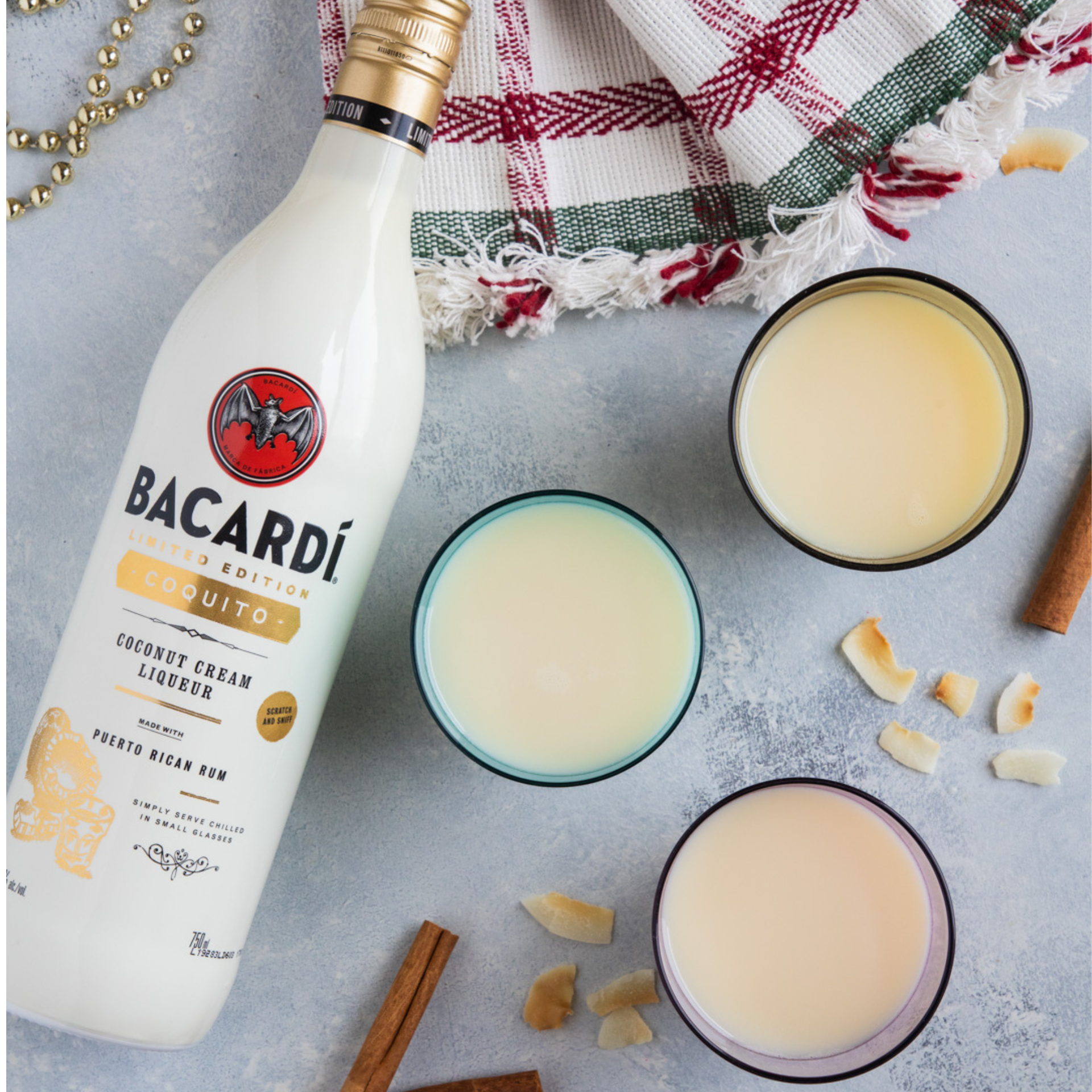 Bottle of Bacardí Coquito Coconut Cream Liqueur with three filled glasses, surrounded by festive holiday decor