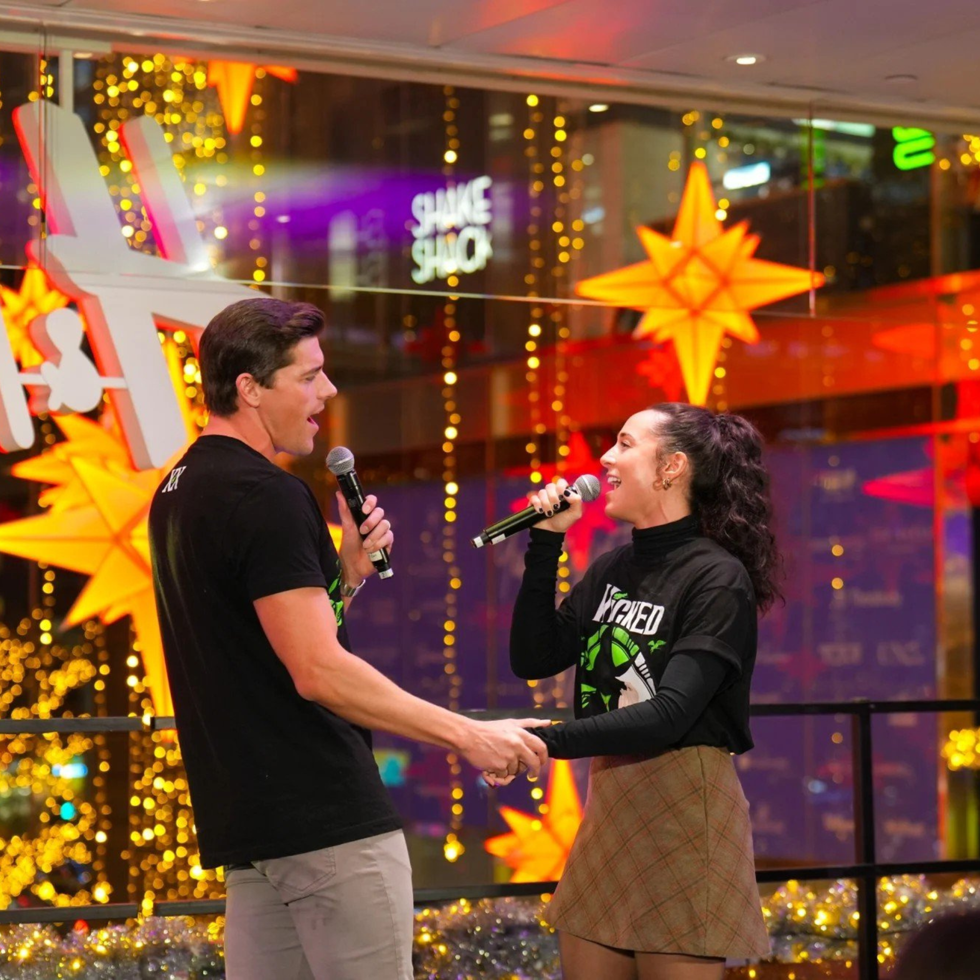 Two people holding microphones and hands while performing in a festive space with star decorations