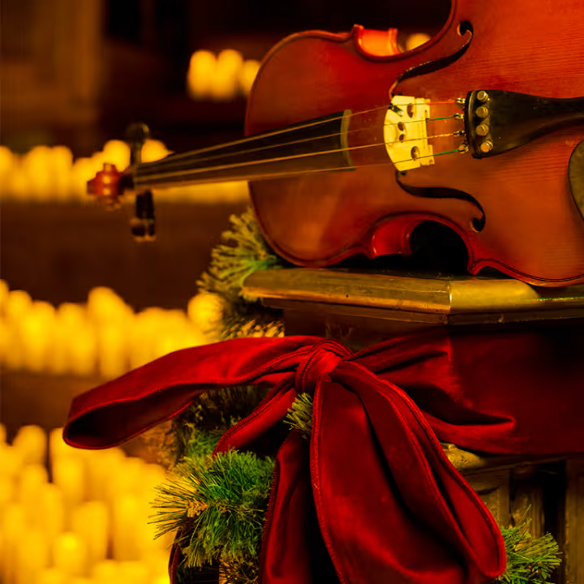 Close-up of a violin on a festive pedestal with pine branches, red ribbon, and glowing candles
