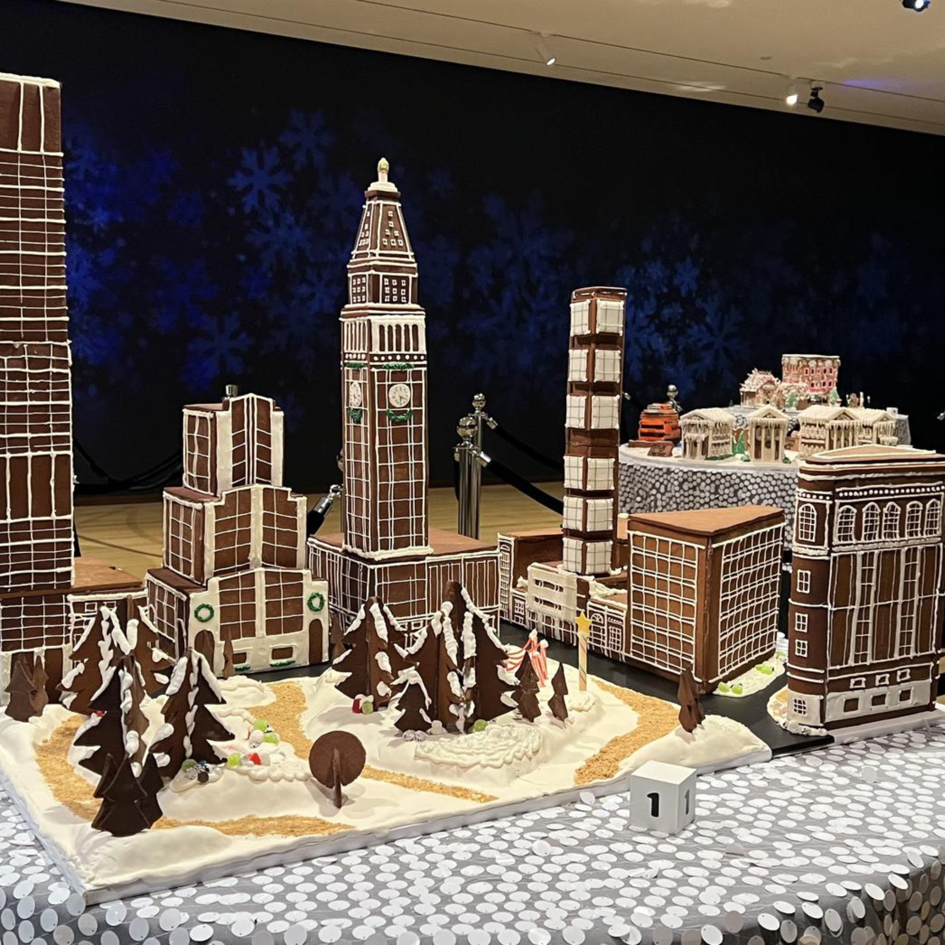 Gingerbread cityscape with iced buildings, snowy trees, and a tall clock tower on a winter-themed base