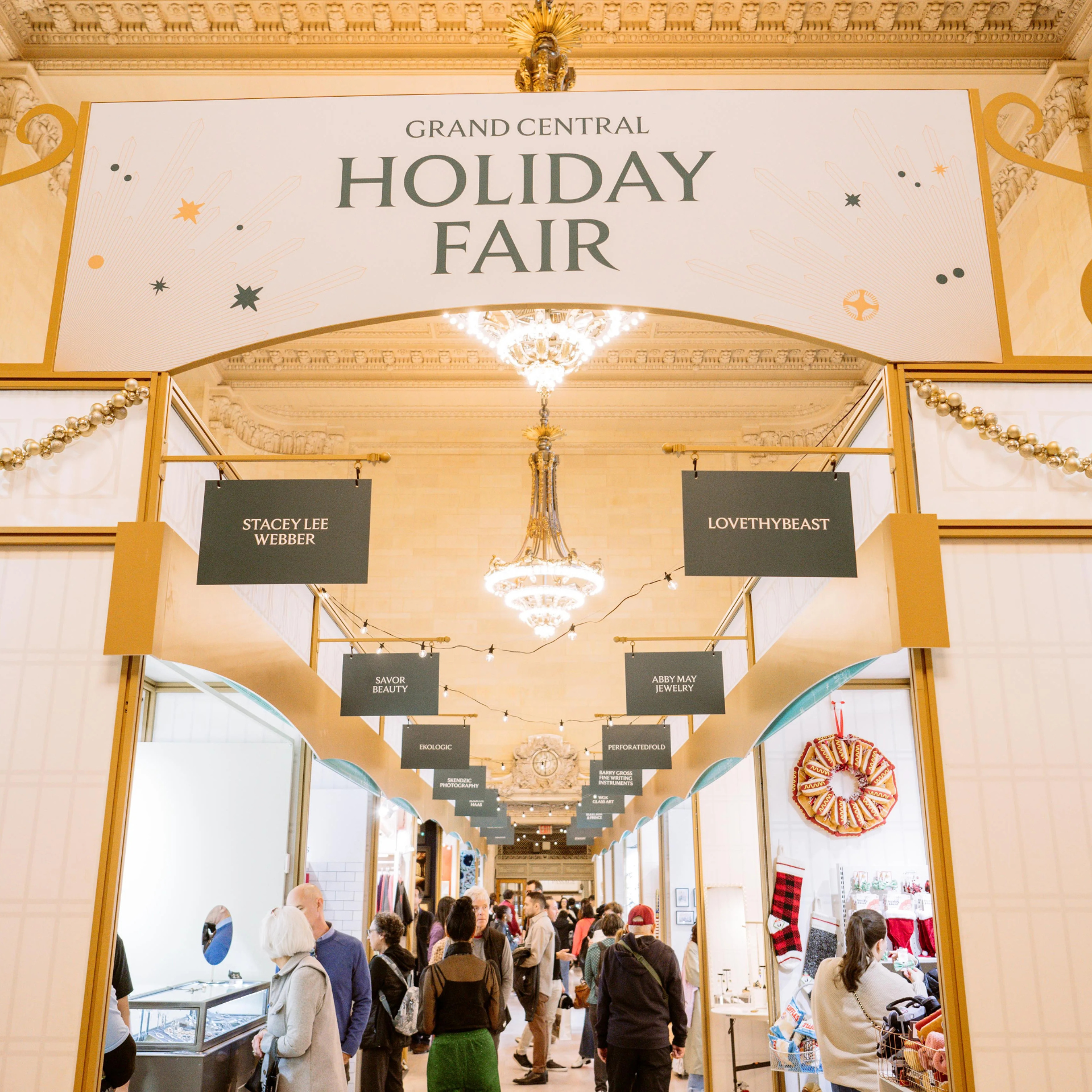 Indoor holiday market at Grand Central Terminal with vendor booths, festive decor, and shoppers browsing
