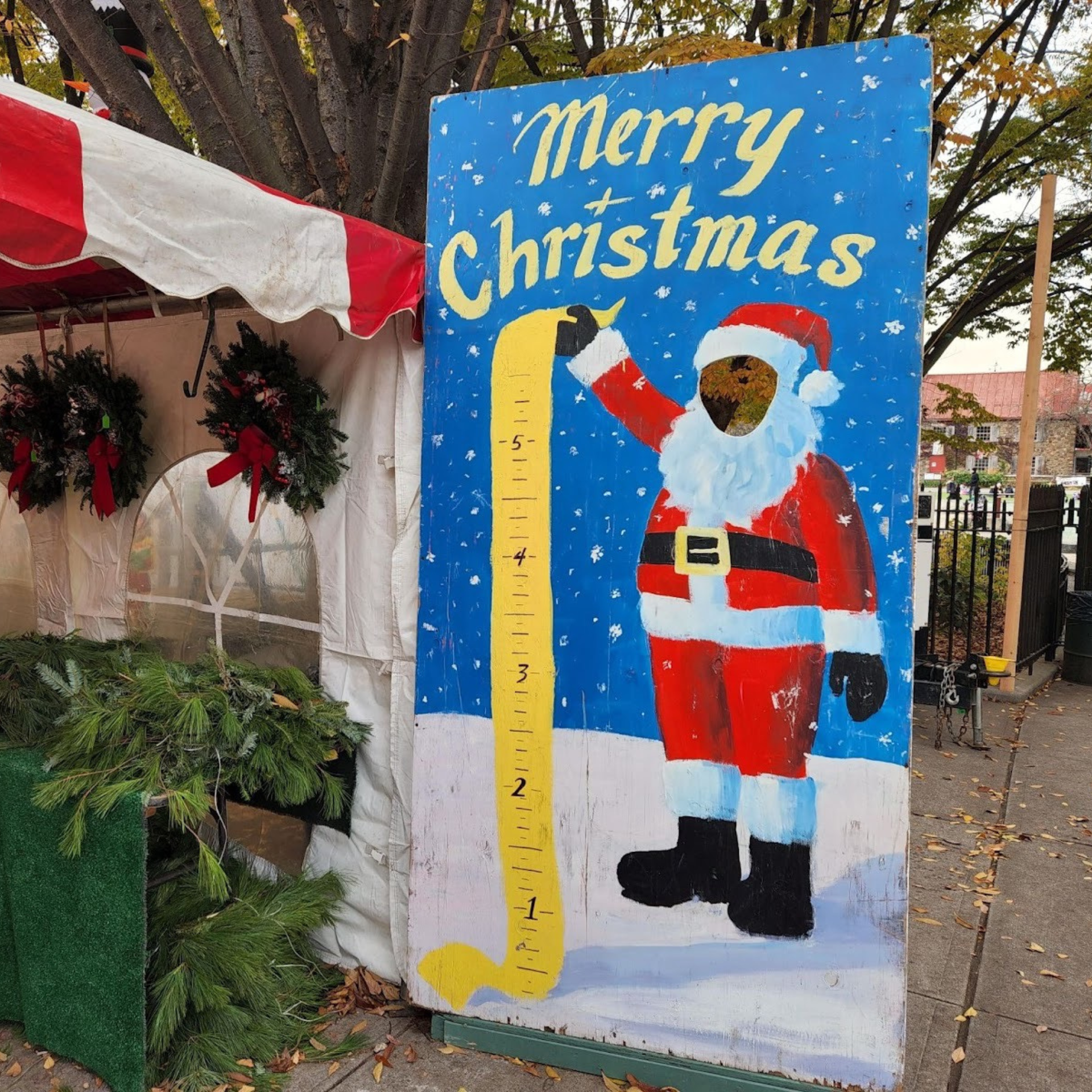 Festive Christmas market scene with a striped tent, holiday wreaths, and a Santa height chart photo board