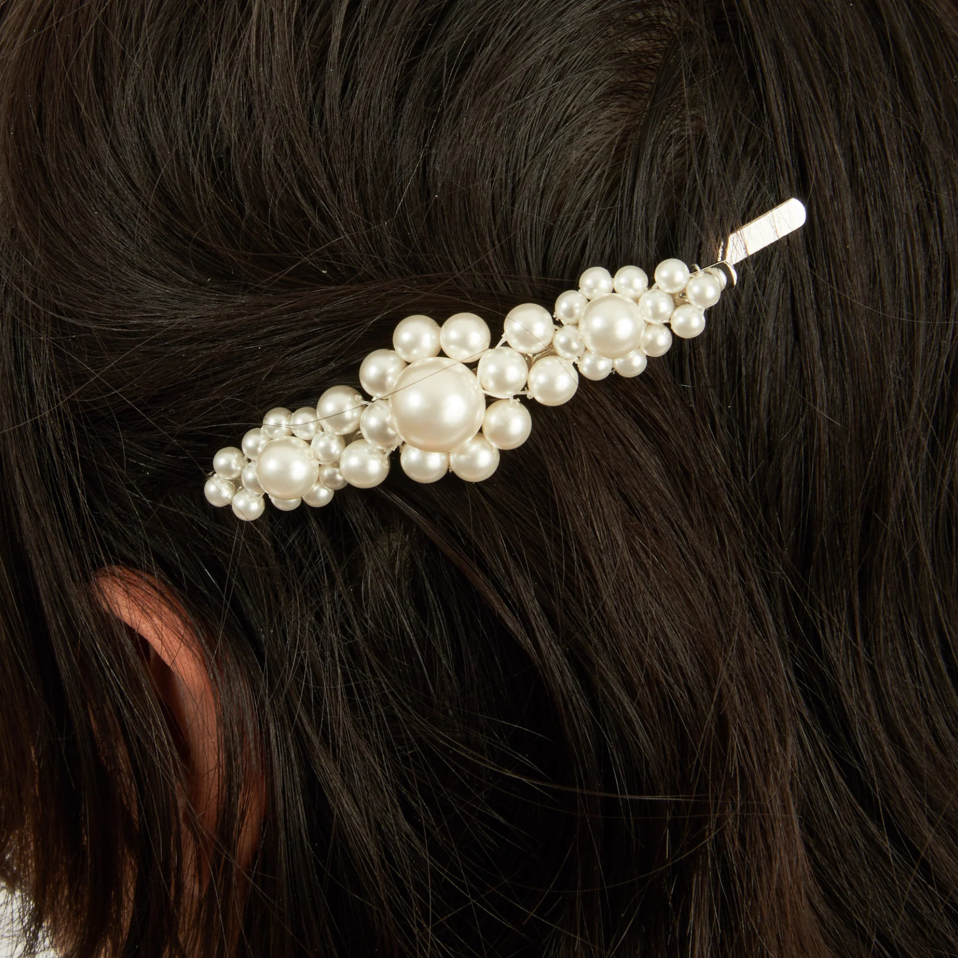 Close-up of dark brown hair with a pearl-studded hair clip featuring clustered white pearls on a metallic base