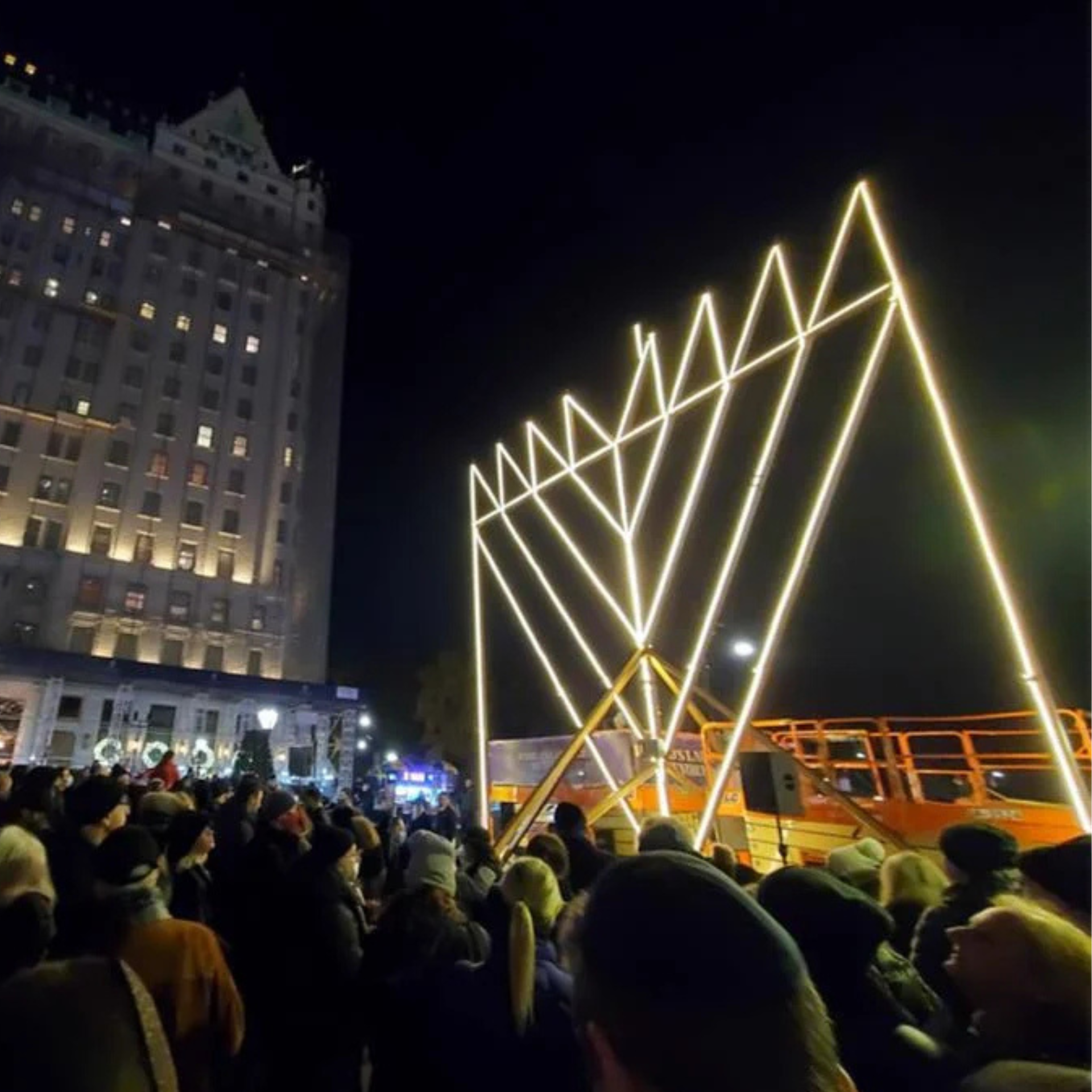 Crowd gathered at night around a giant illuminated menorah for a public Hanukkah celebration