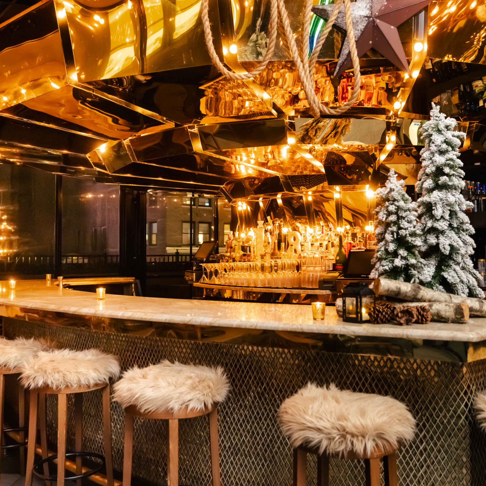 Elegant bar with marble counter, fur-covered stools, and festive winter decorations including pine trees and lantern
