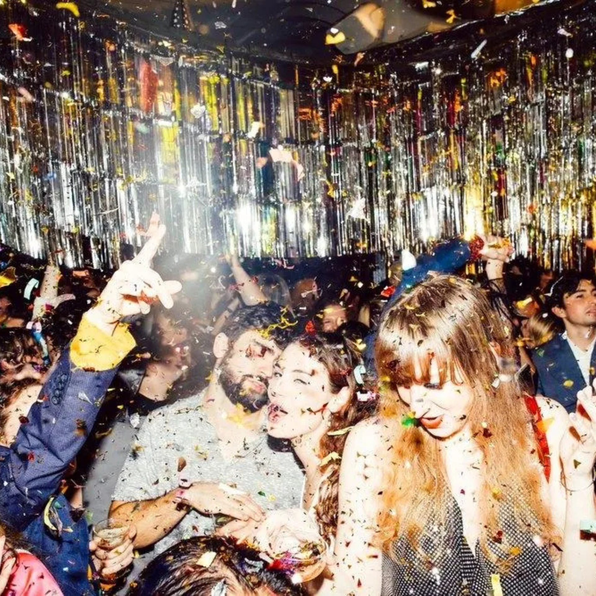 Crowd dancing under metallic streamers and falling confetti at a vibrant indoor party