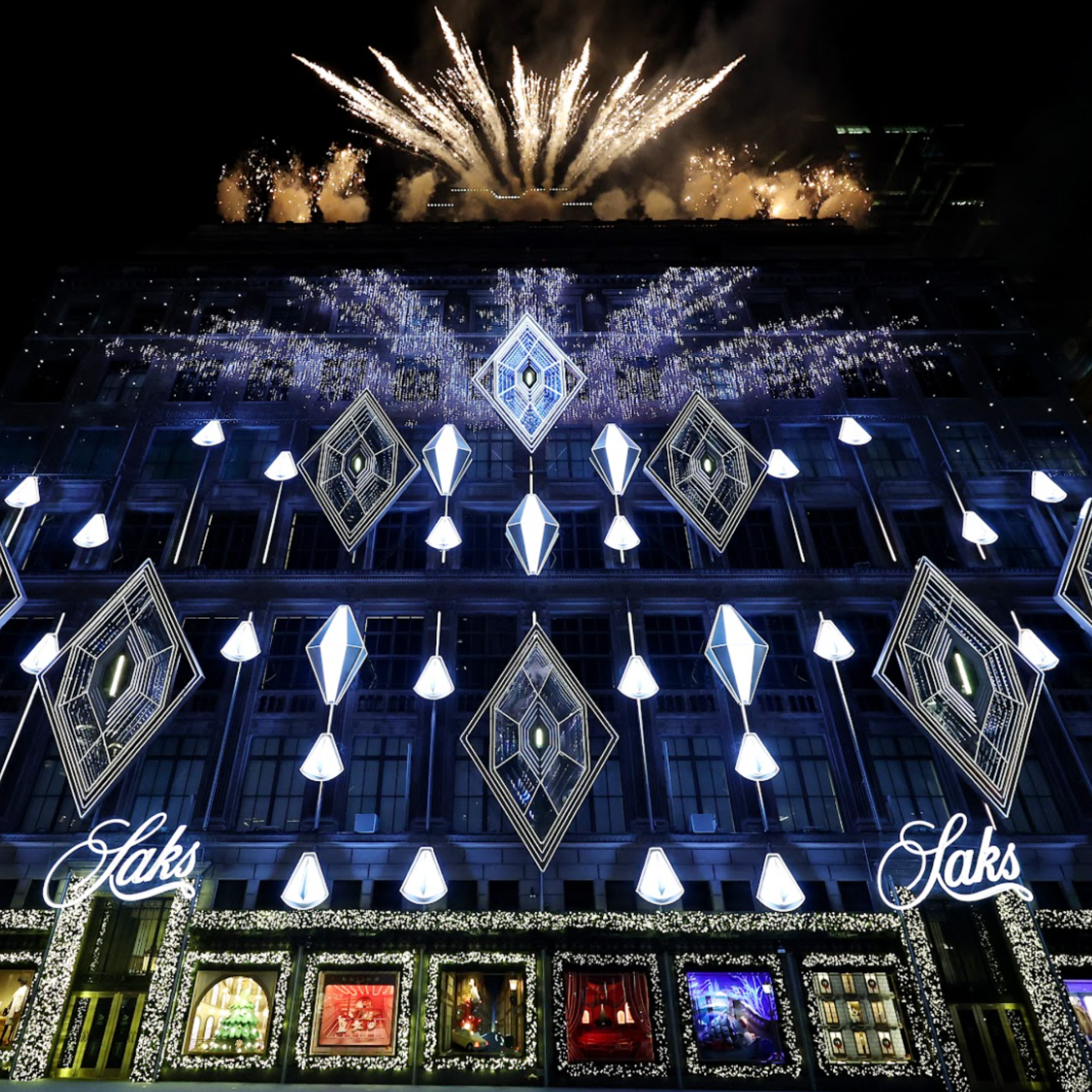 Saks Fifth Avenue building lit up with holiday lights, sparkling decorations, and festive window displays at night