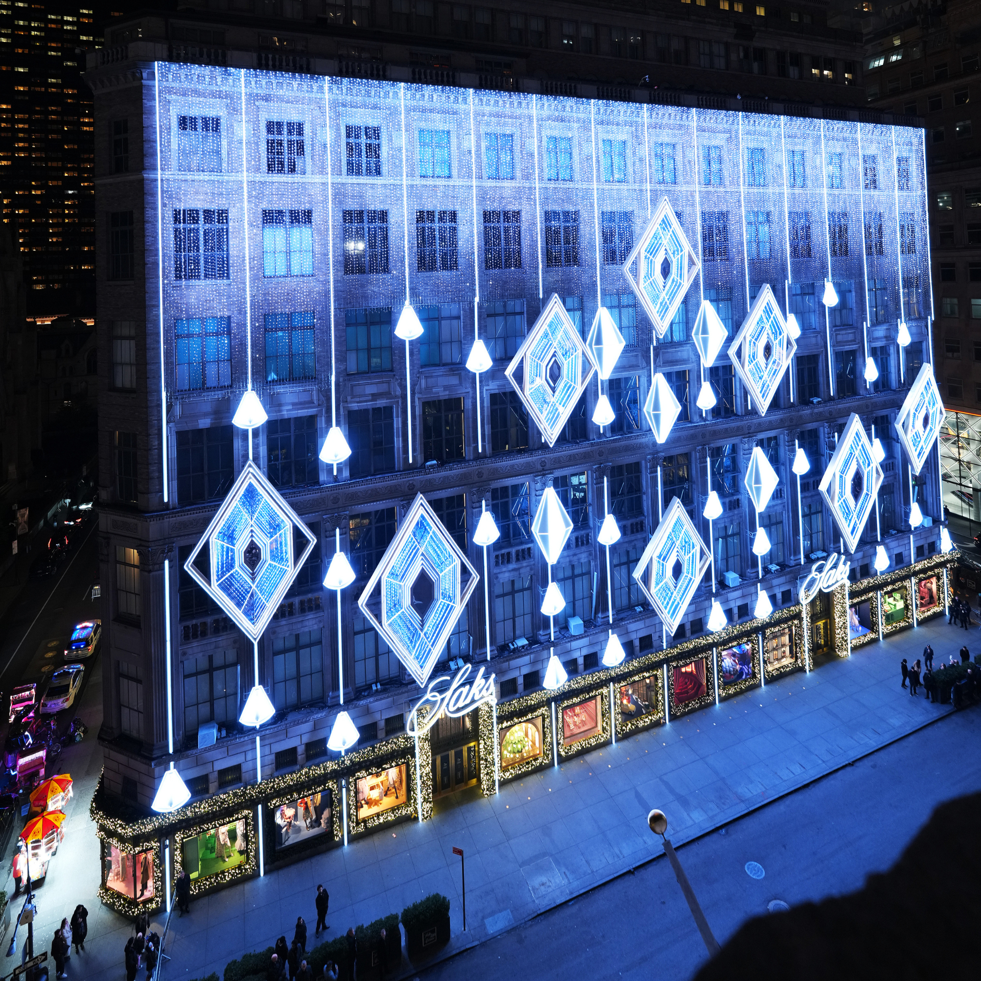 Saks Fifth Avenue storefront at night, glowing with holiday lights, garlands, and festive window displays
