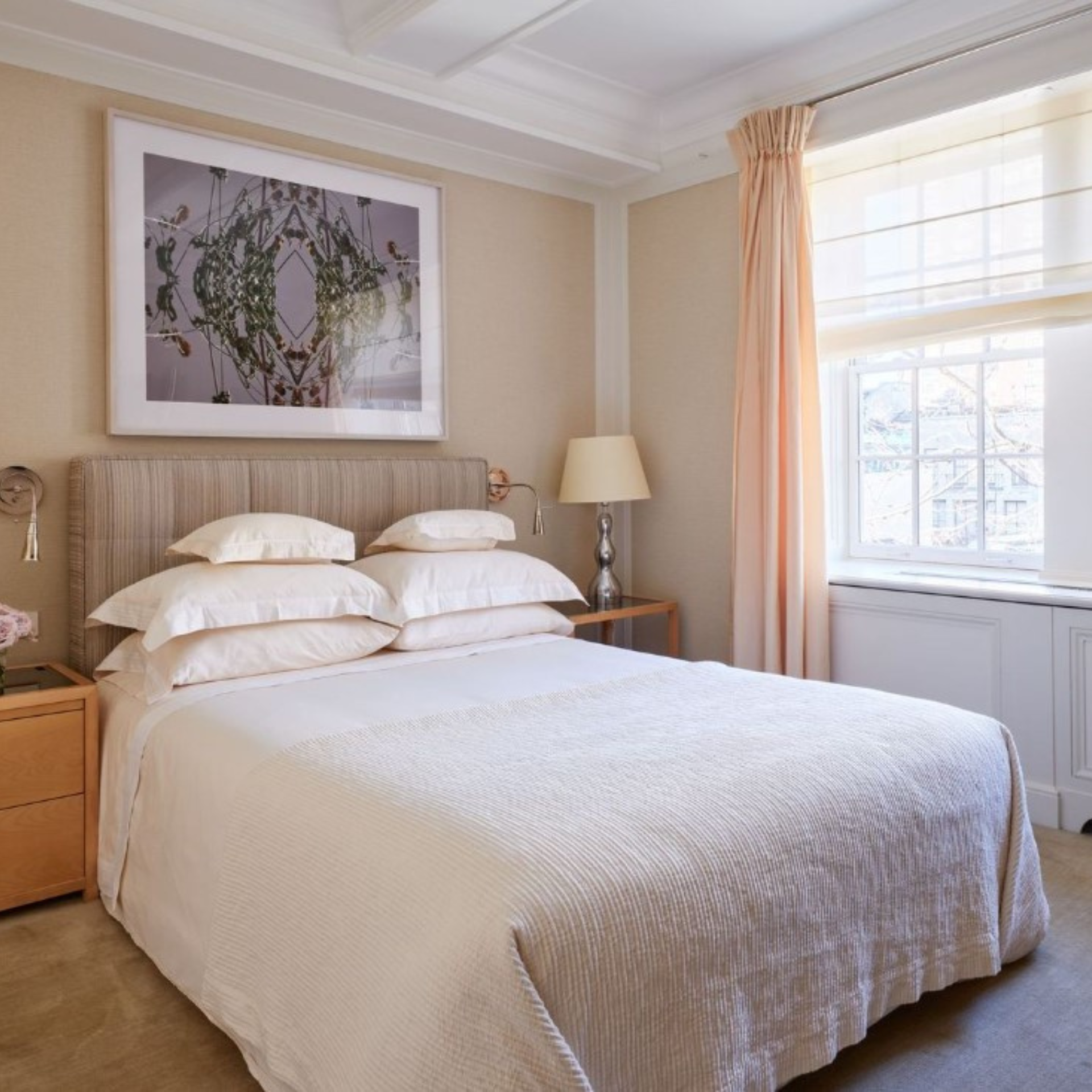 Elegant bedroom with white linens, beige headboard, floral decor, and botanical artwork above the bed