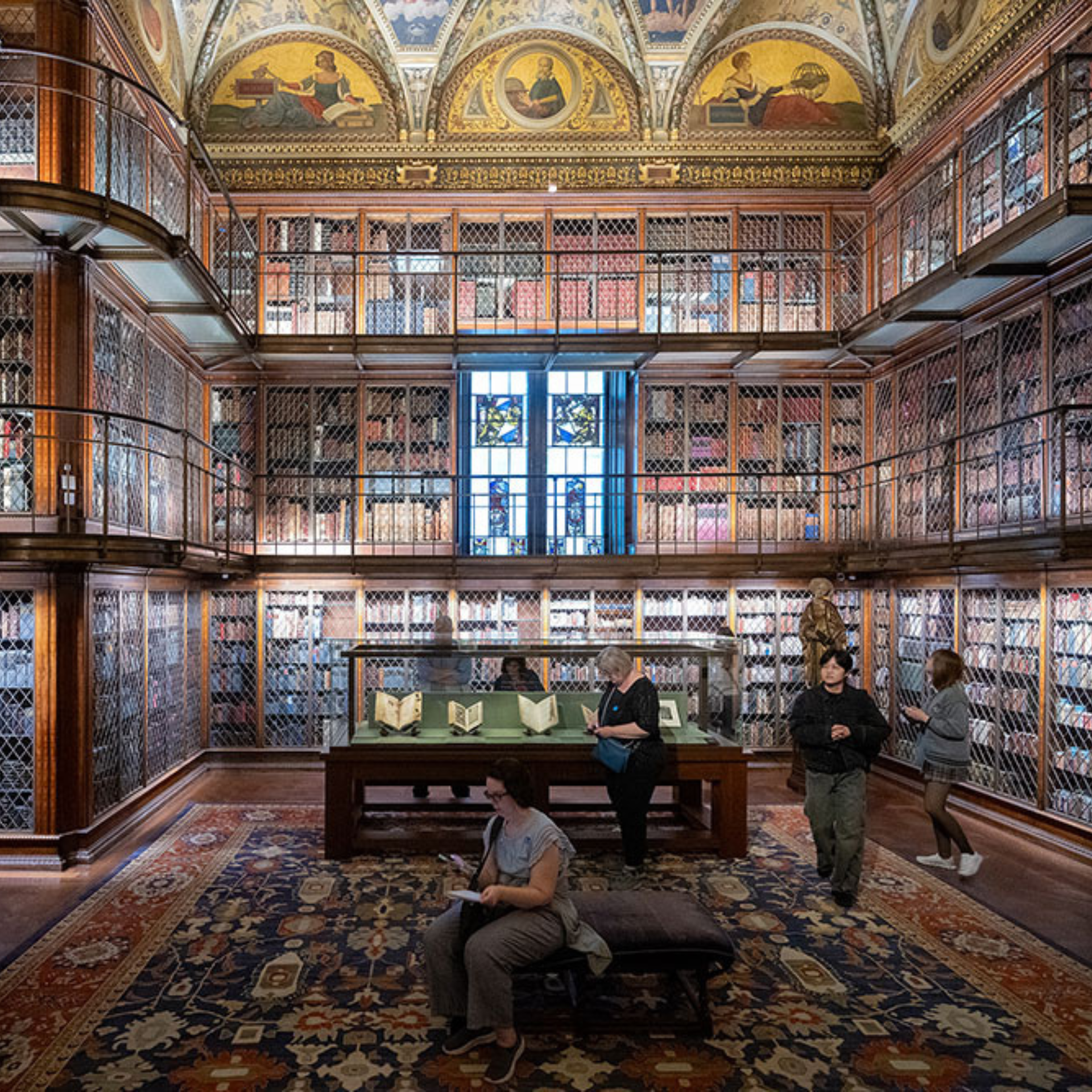 Interior of the Morgan Library in New York City with frescoed ceiling, tall wooden bookshelves, stained glass, and rare manuscripts on display