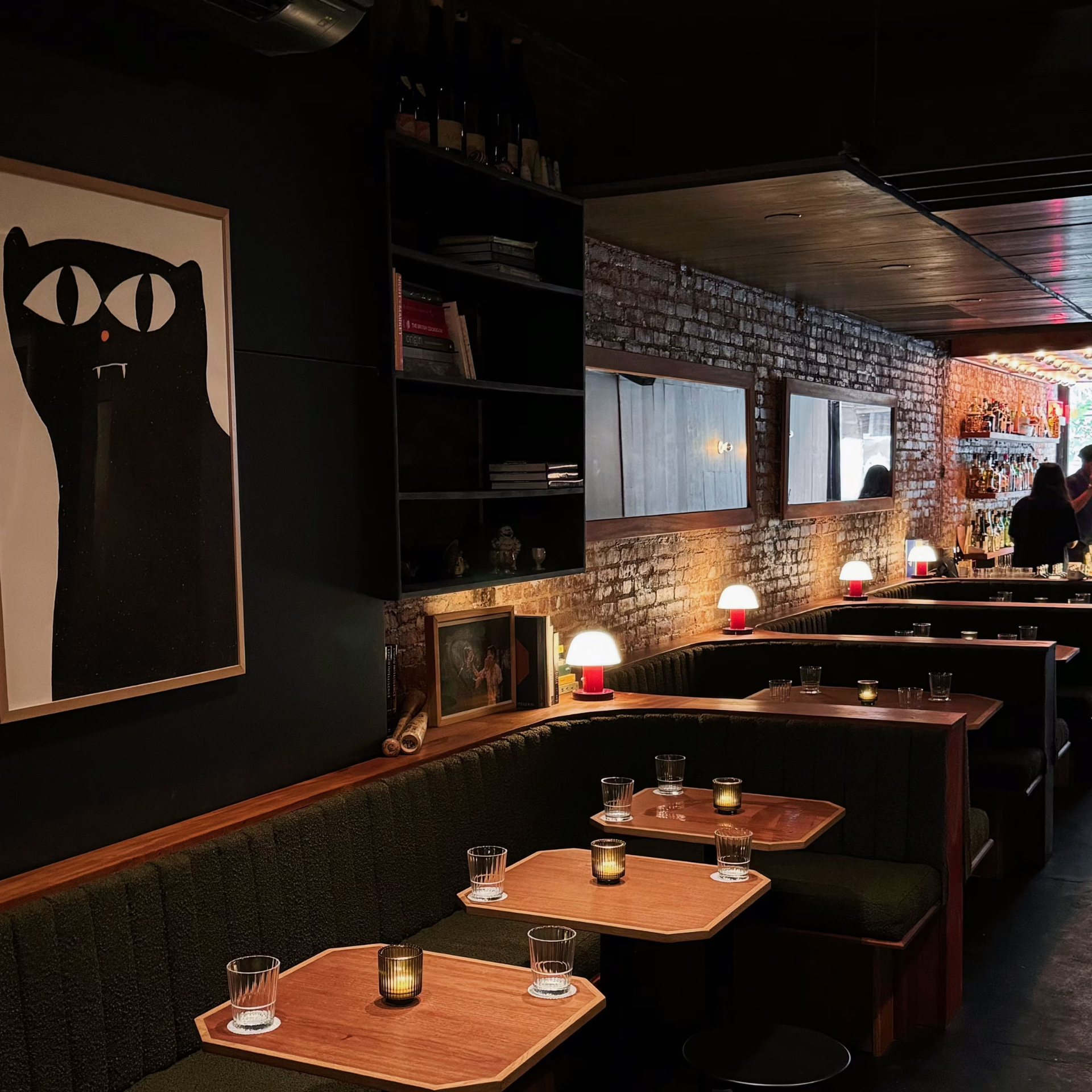 Dimly lit bar with green booths, exposed brick walls, eclectic artwork, and warm candlelit tables