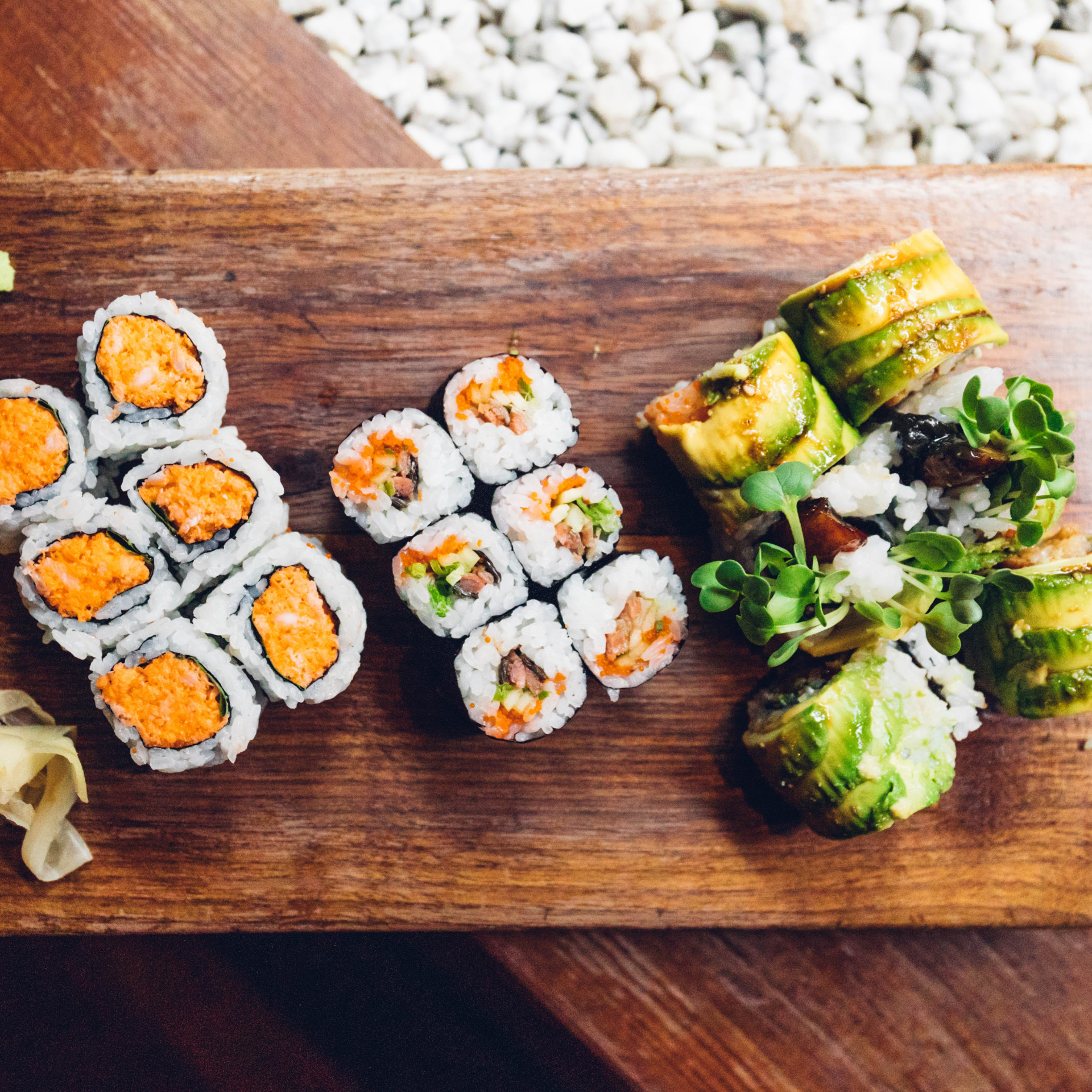 Sushi rolls with spicy tuna, vegetable maki, and avocado-wrapped rolls garnished with microgreens on a wooden board