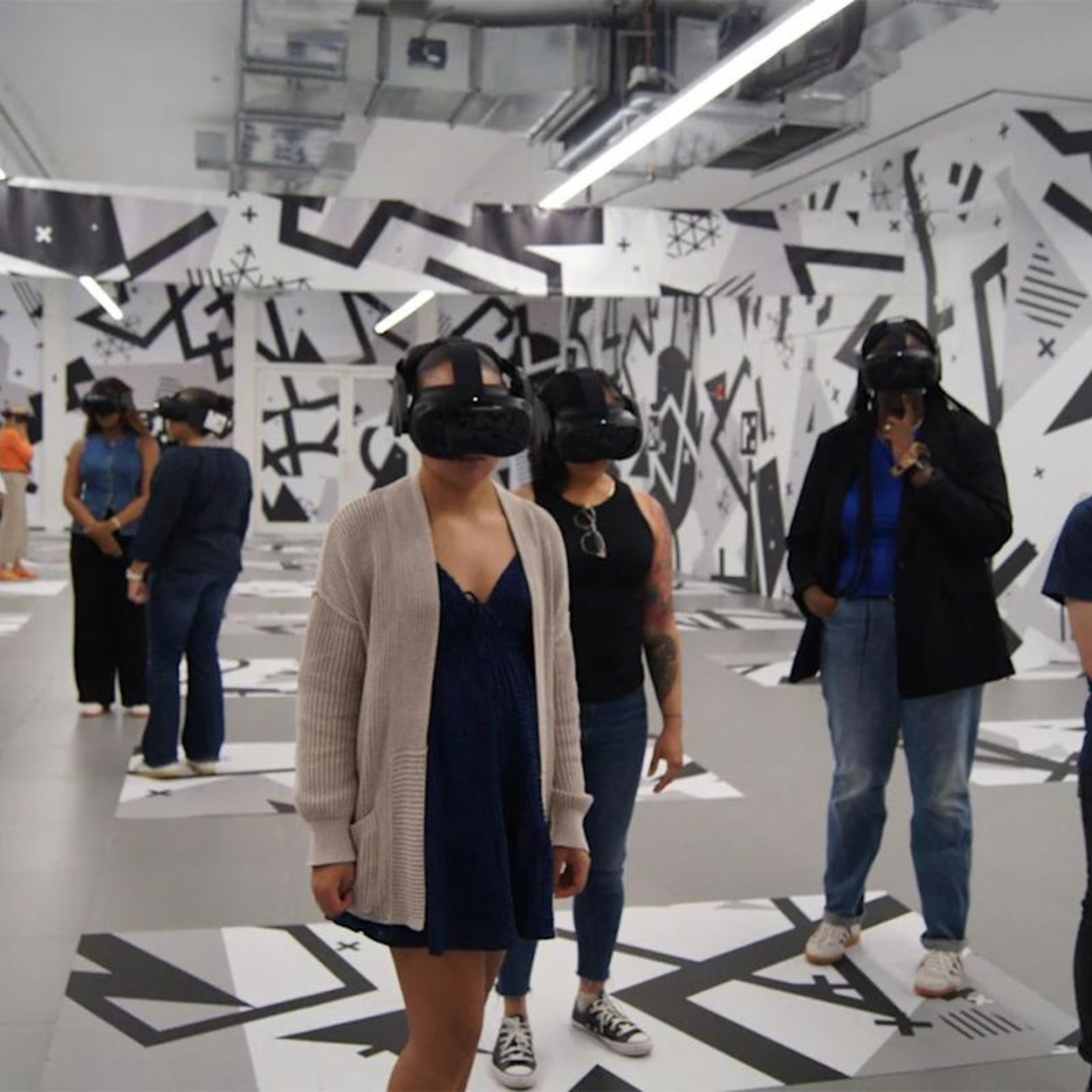 Group of people wearing VR headsets in a modern exhibition space with geometric black-and-white wall art