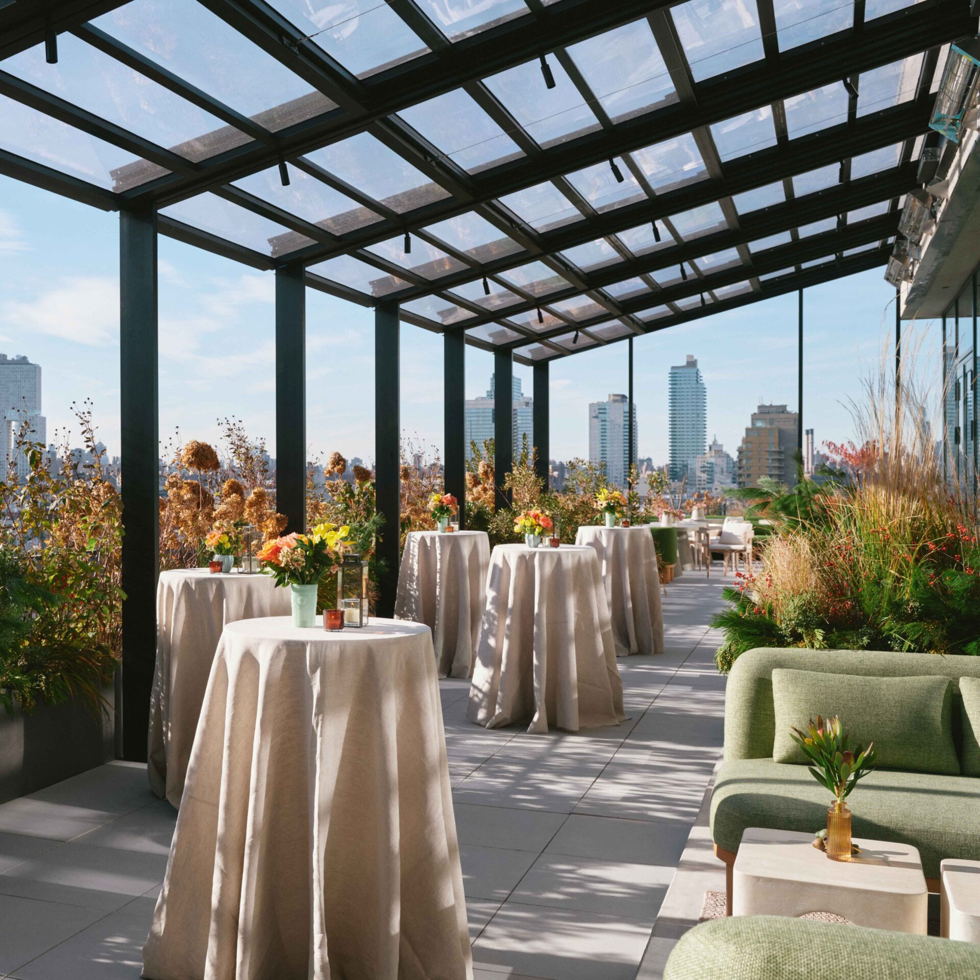 Stylish rooftop terrace with glass roof, cocktail tables, floral centerpieces, and city skyline views