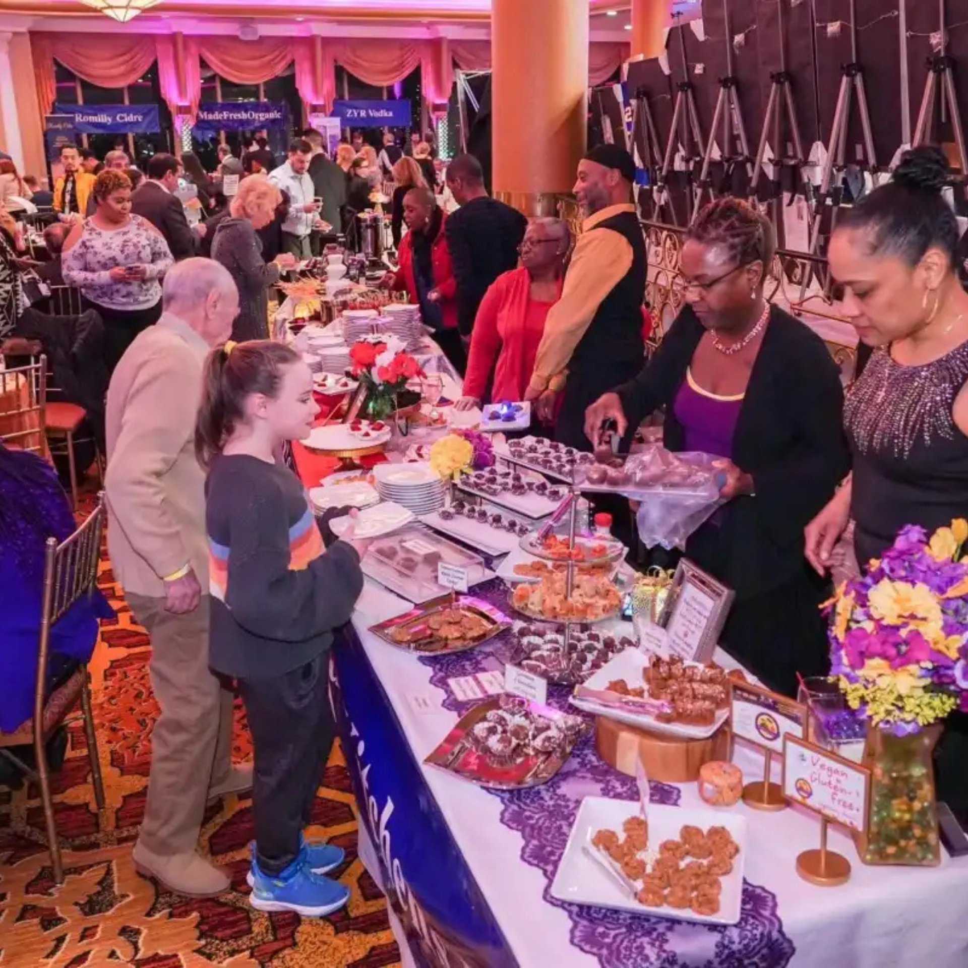 Crowd enjoying a dessert showcase at a festive indoor culinary event, with tables of cakes, cookies, and chocolates under warm lighting