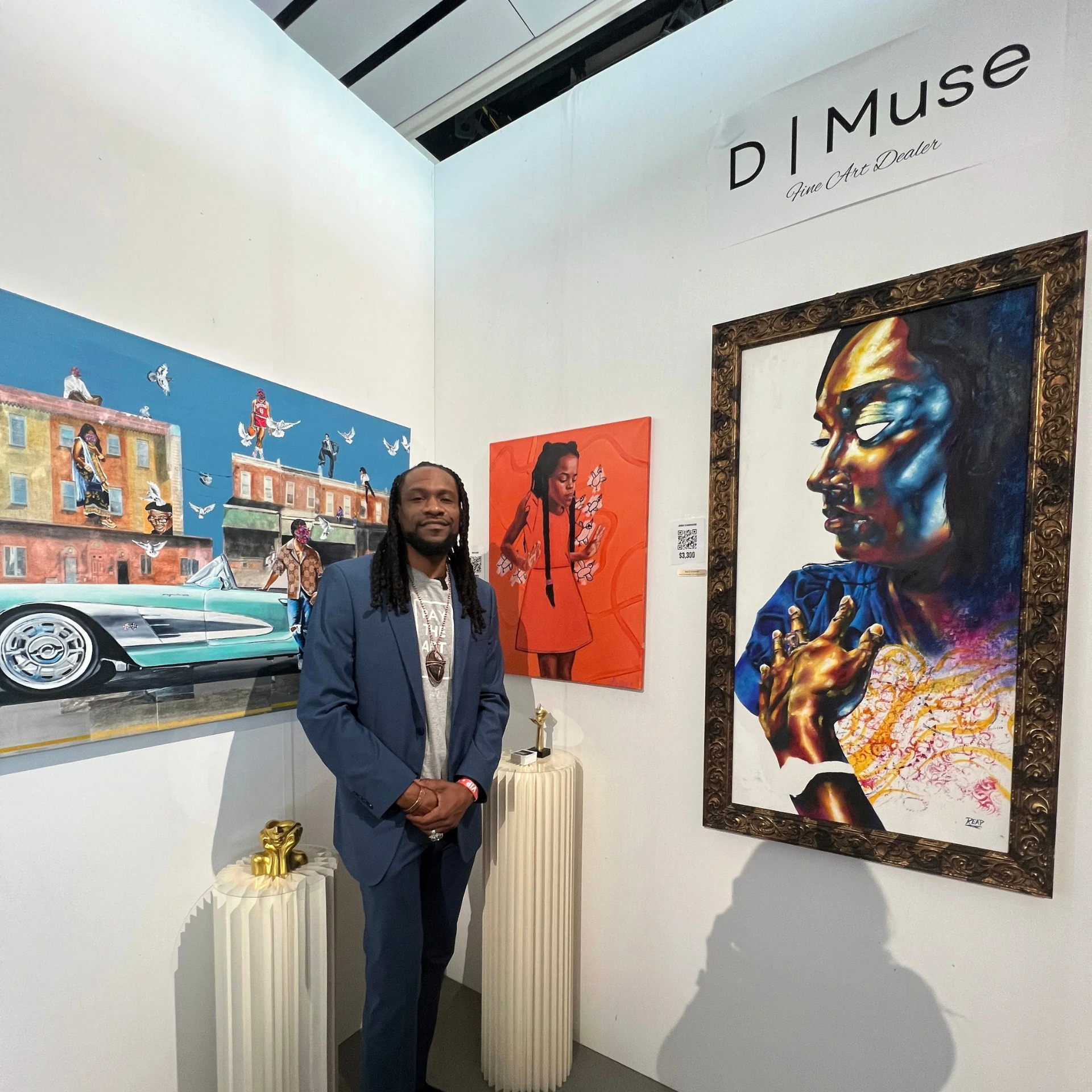 Man in a blue suit standing in front of colorful paintings at an art gallery display labeled “D Muse Fine Art Dealer