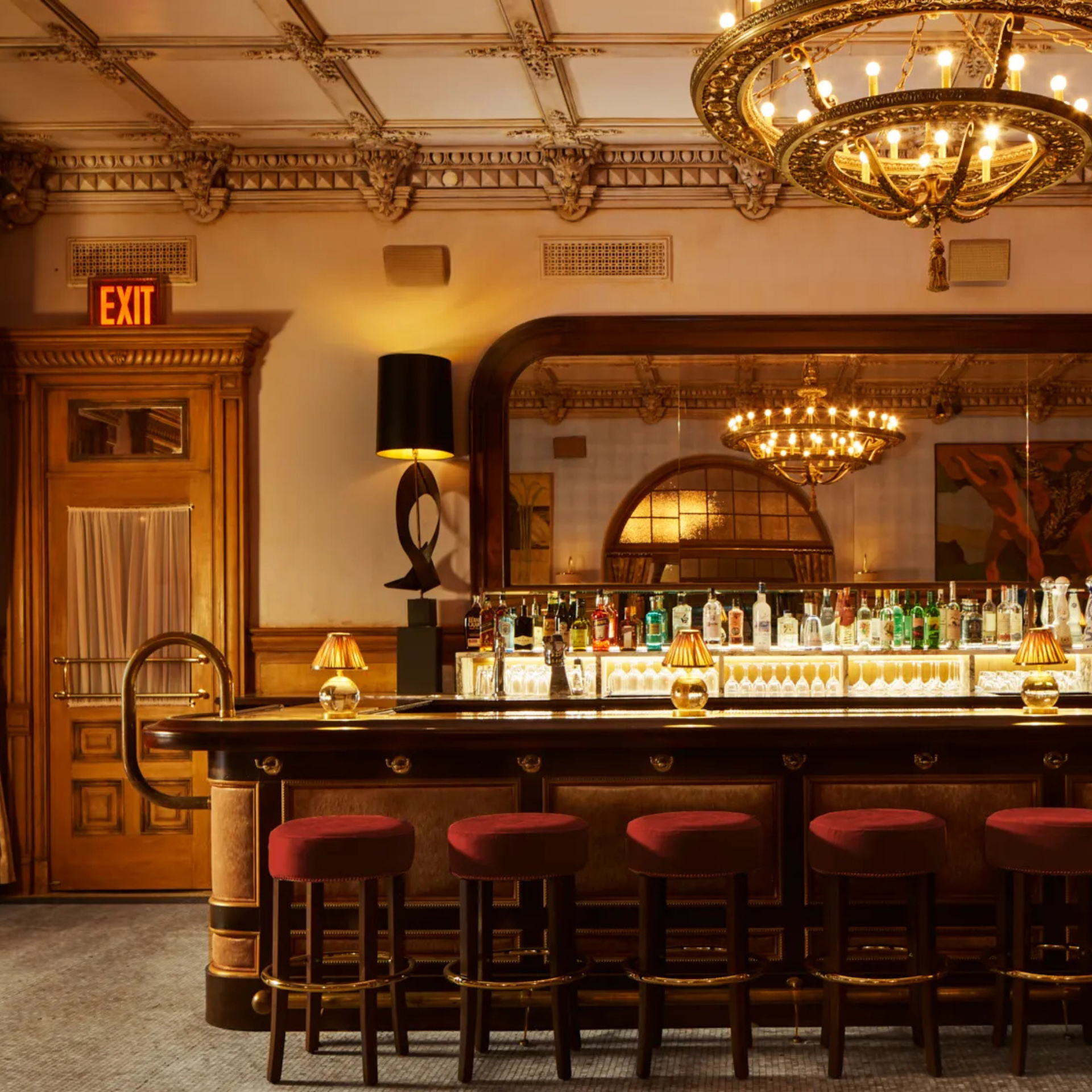 Luxurious vintage-style bar with red stools, golden lamps, chandelier, and mirrored backdrop