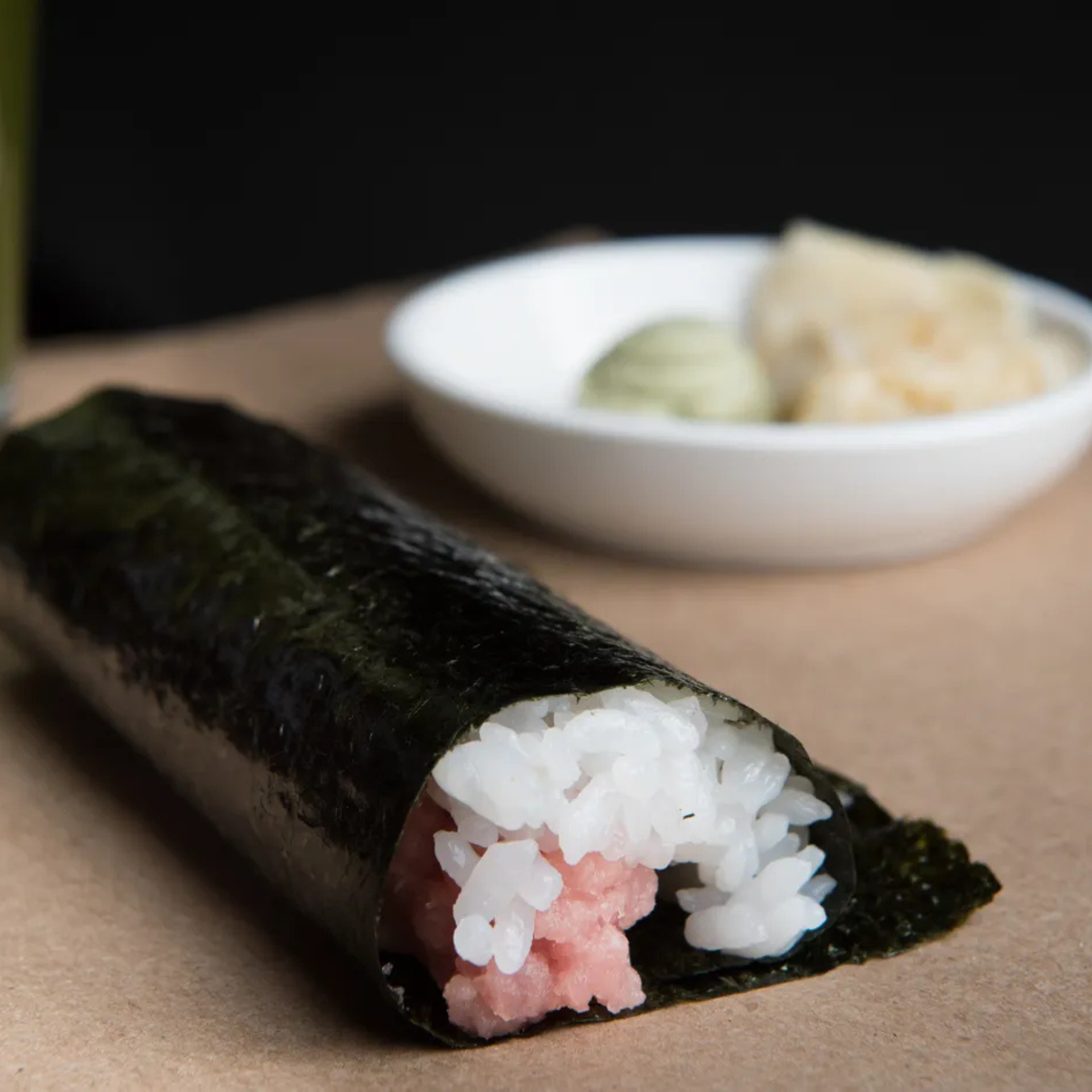 Tuna hand roll sushi wrapped in nori with rice, served alongside wasabi and pickled ginger
