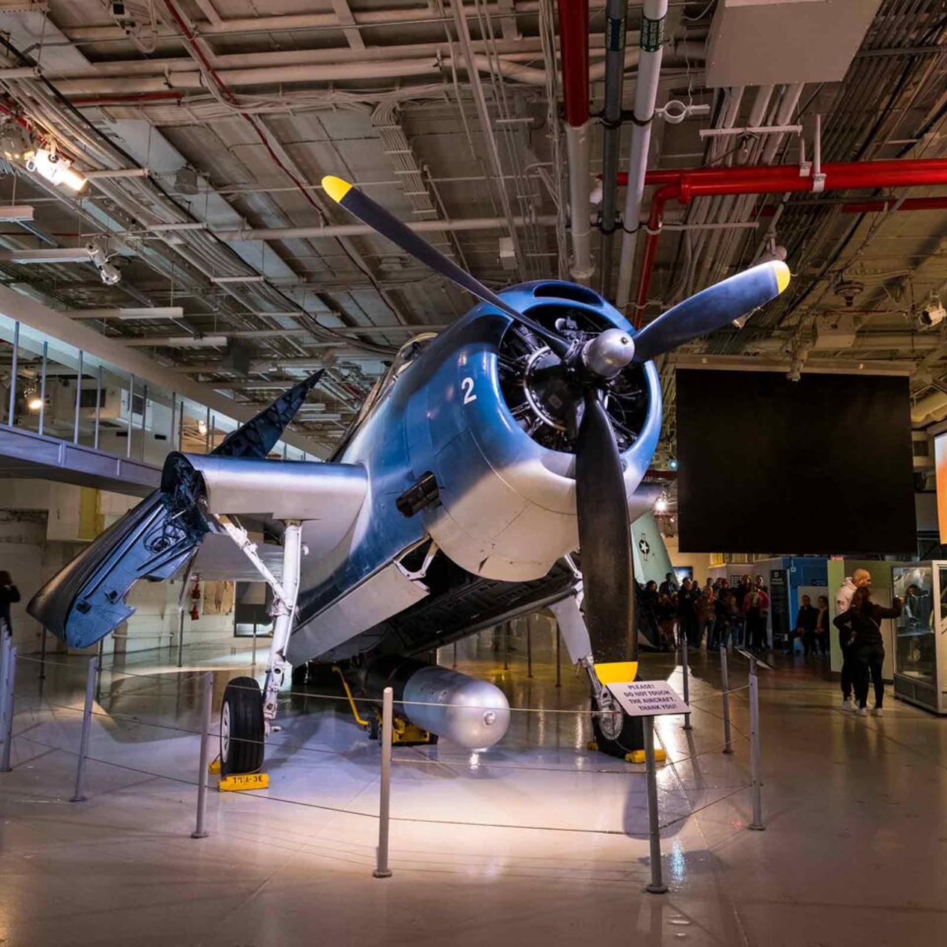Vintage blue and white military aircraft with propeller and mounted torpedo on display in aviation museum