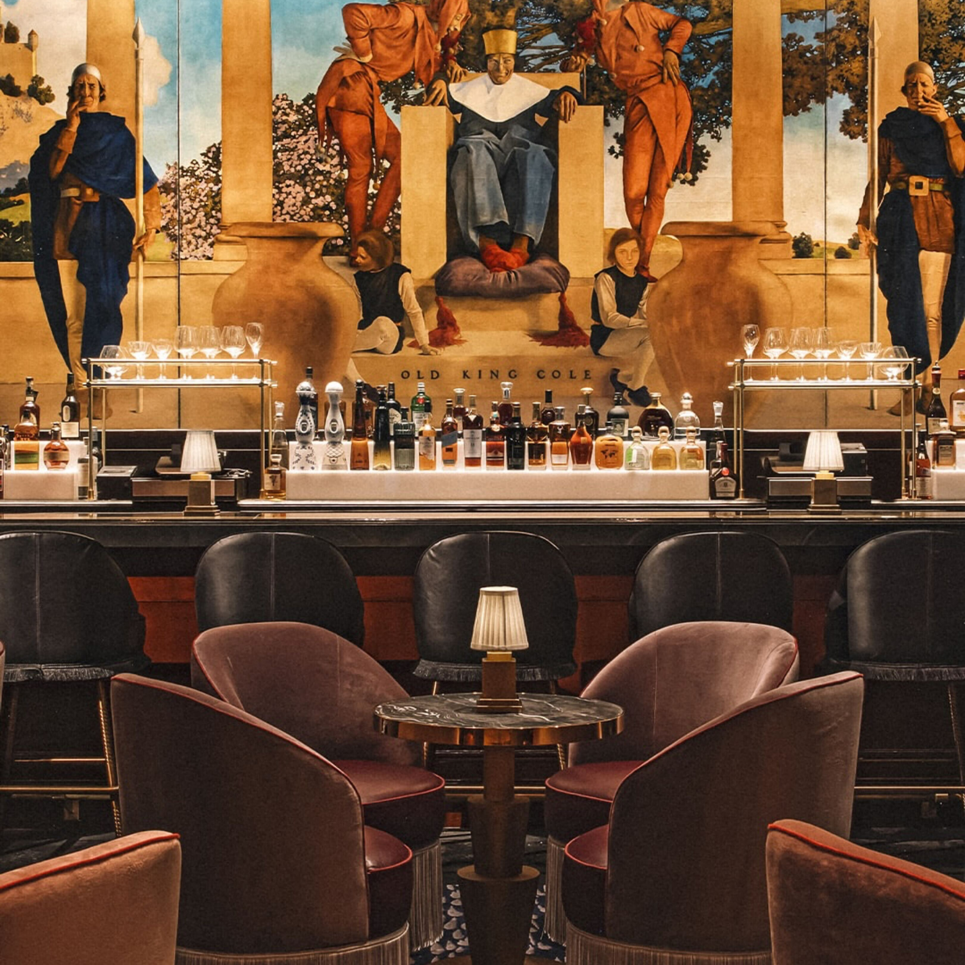 Elegant bar interior with mural of Old King Cole behind a well-stocked counter and plush seating