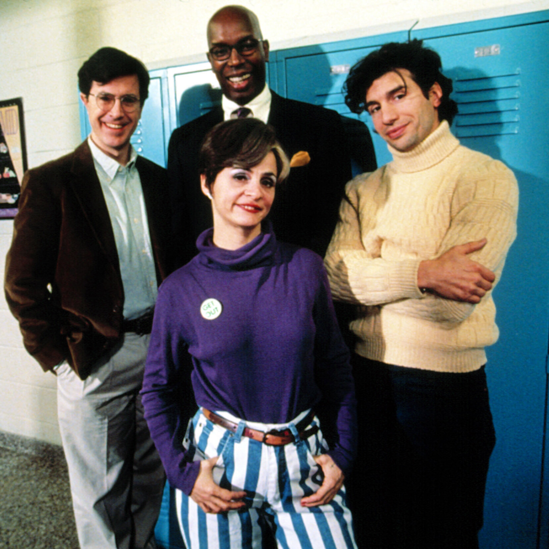 Four adults in casual and semi-formal outfits posing in front of blue school lockers.