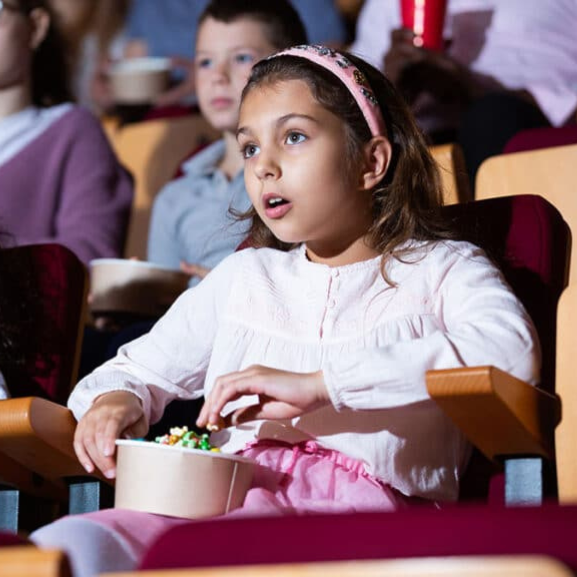 Young girl with popcorn watching a show in a theater, surrounded by other captivated audience members