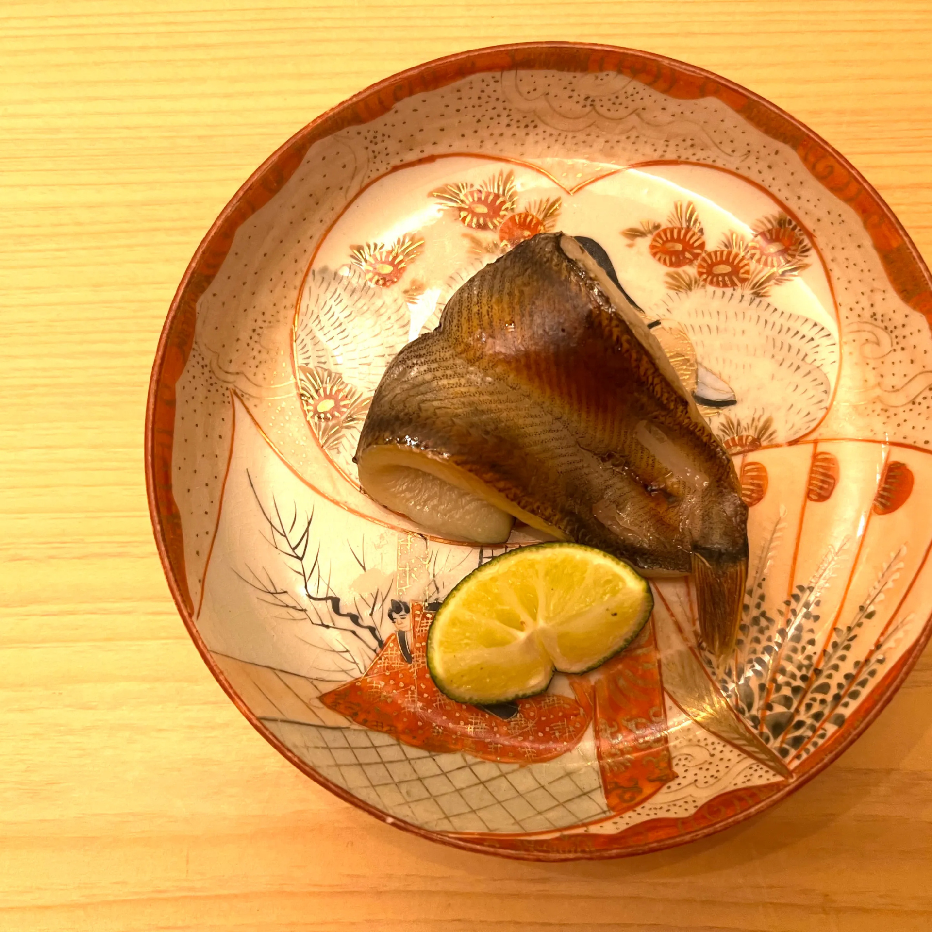 Grilled fish with lime served on a decorative Japanese ceramic plate with traditional artwork