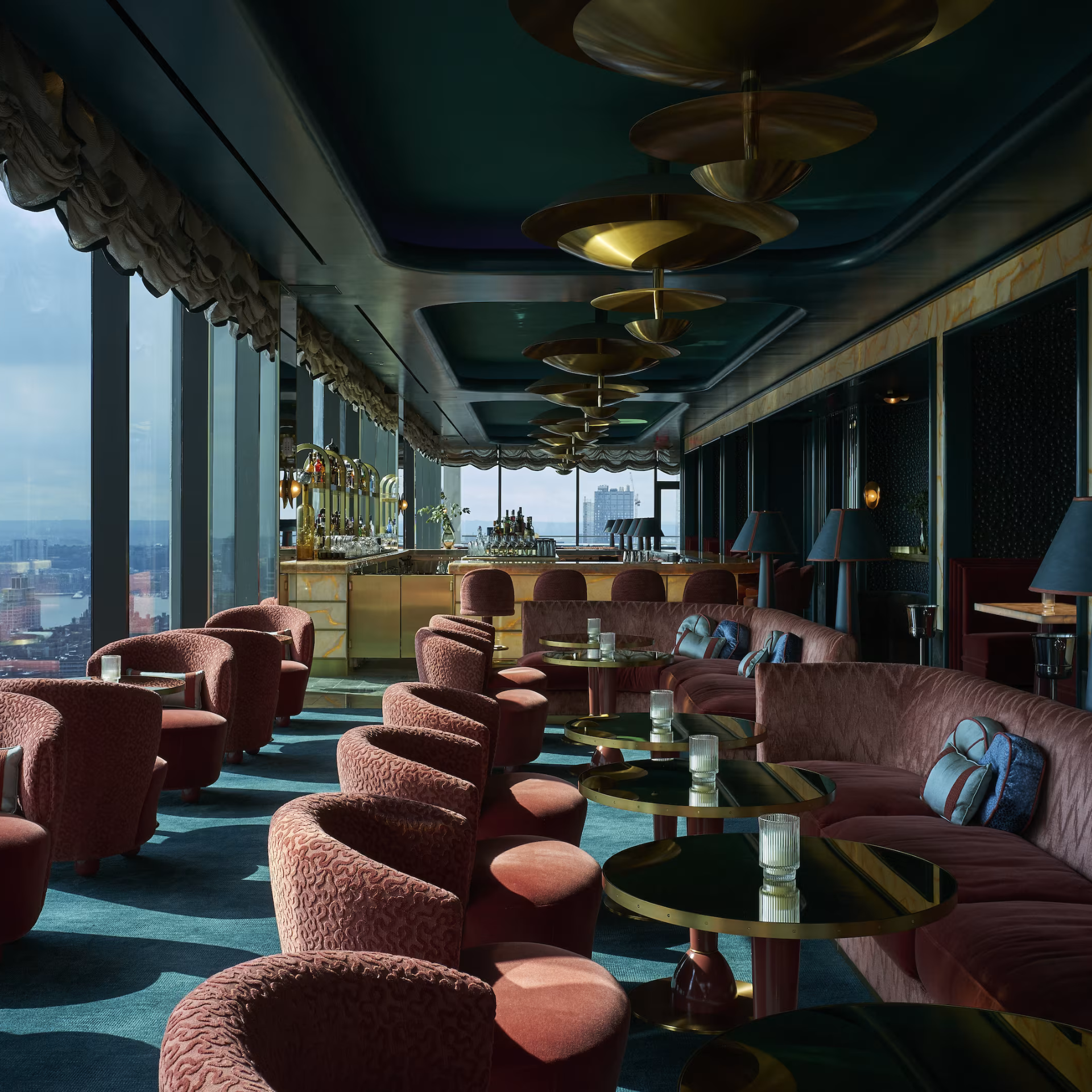 Upscale lounge with burgundy seating, gold light fixtures, and panoramic city views through floor-to-ceiling windows