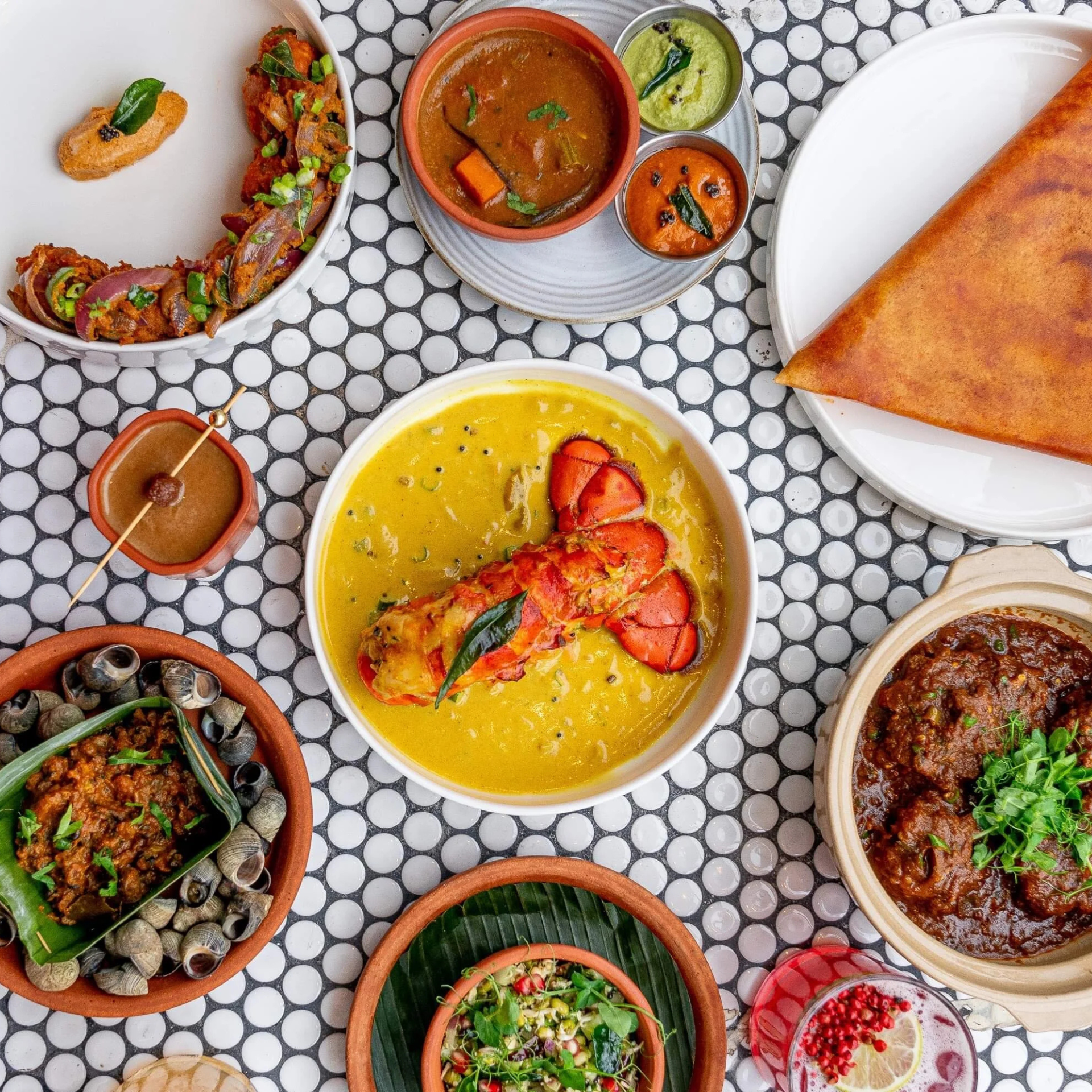 Assorted Indian cuisine platter with lobster curry, dosa, meat curry, snails, salad, skewers, and gulab jamun dessert