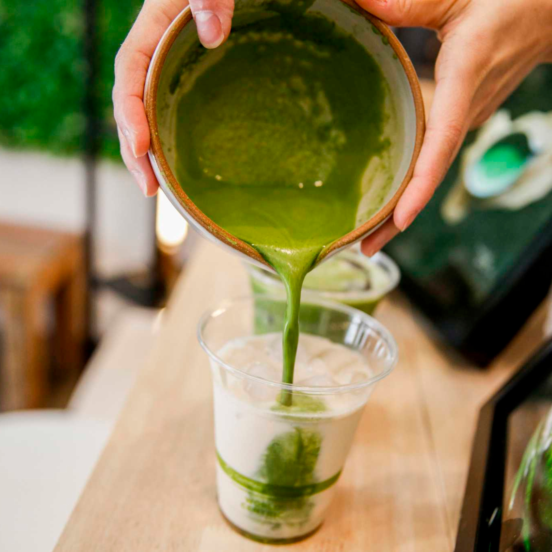 Close-up of matcha being poured over iced milk in a café setting