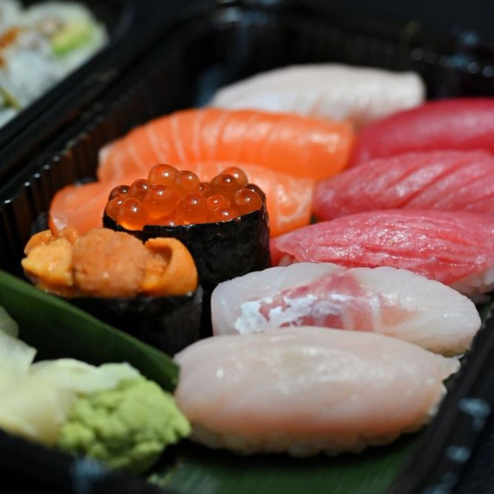 Assorted sushi tray with salmon, tuna, white fish nigiri, gunkan maki with salmon roe and sea urchin, served with wasabi and ginger