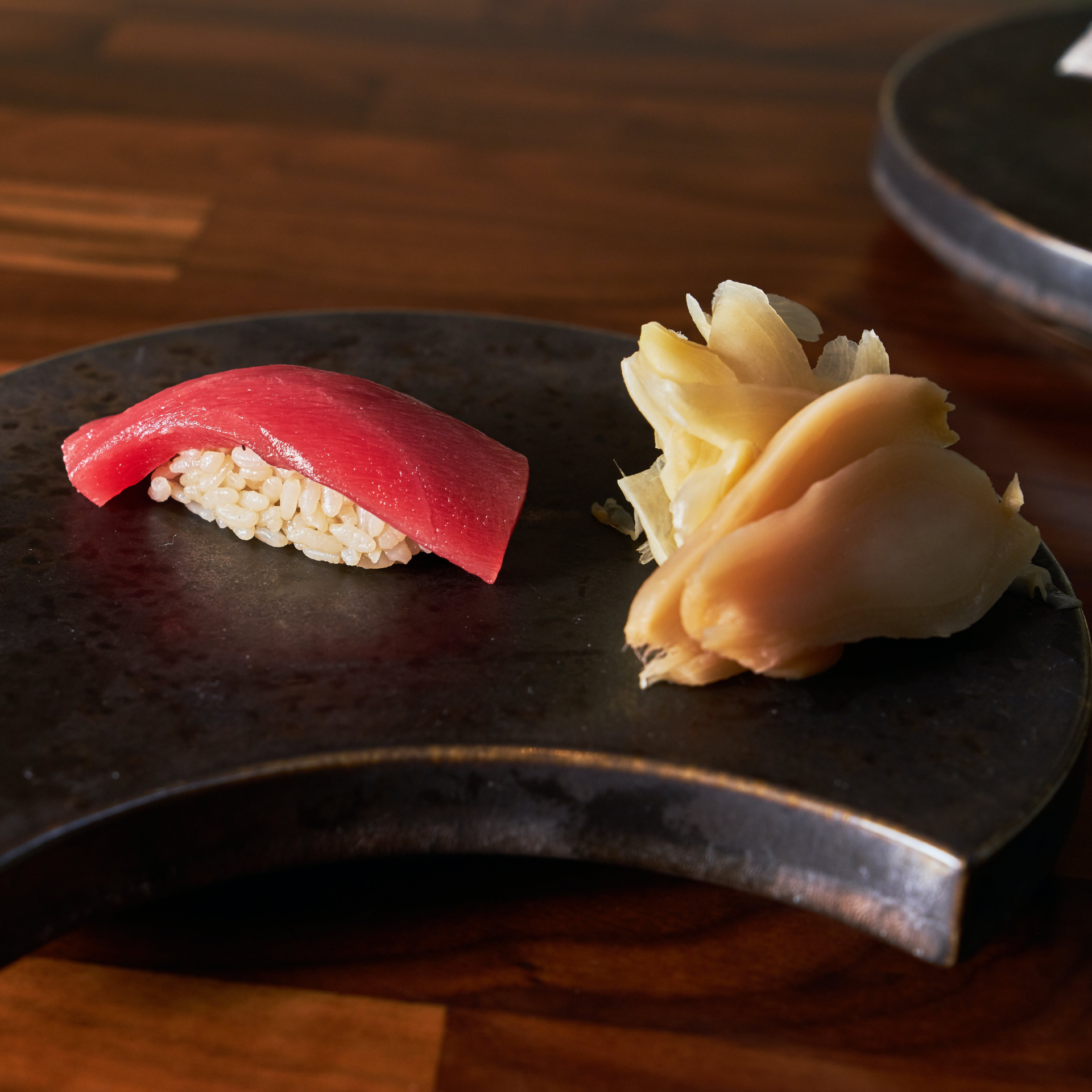 Tuna nigiri sushi with pickled ginger served on a dark ceramic plate