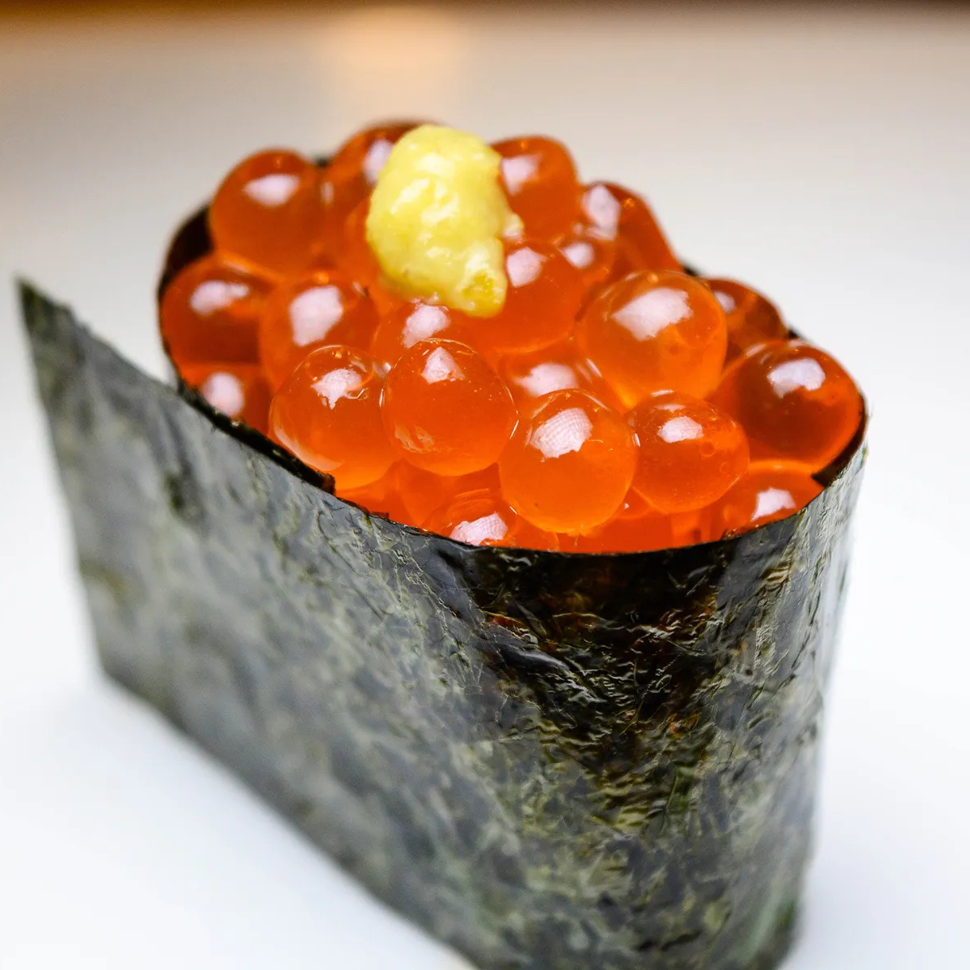 Ikura sushi with bright orange salmon roe on rice, wrapped in seaweed and topped with wasabi