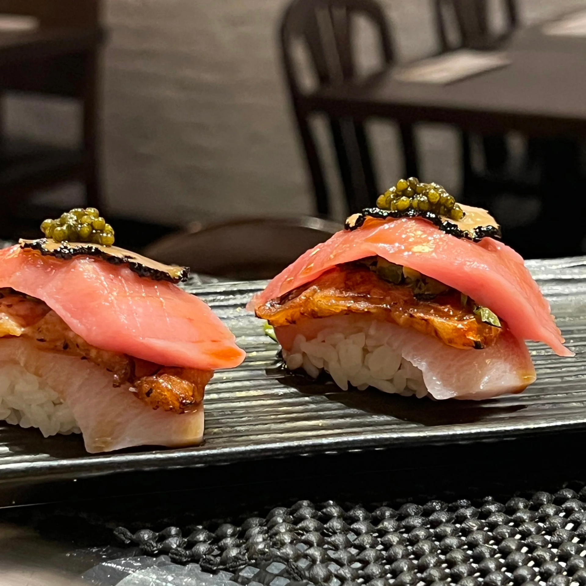 Gourmet sushi with grilled fish, tuna, green caviar, and black truffle on a textured black plate
