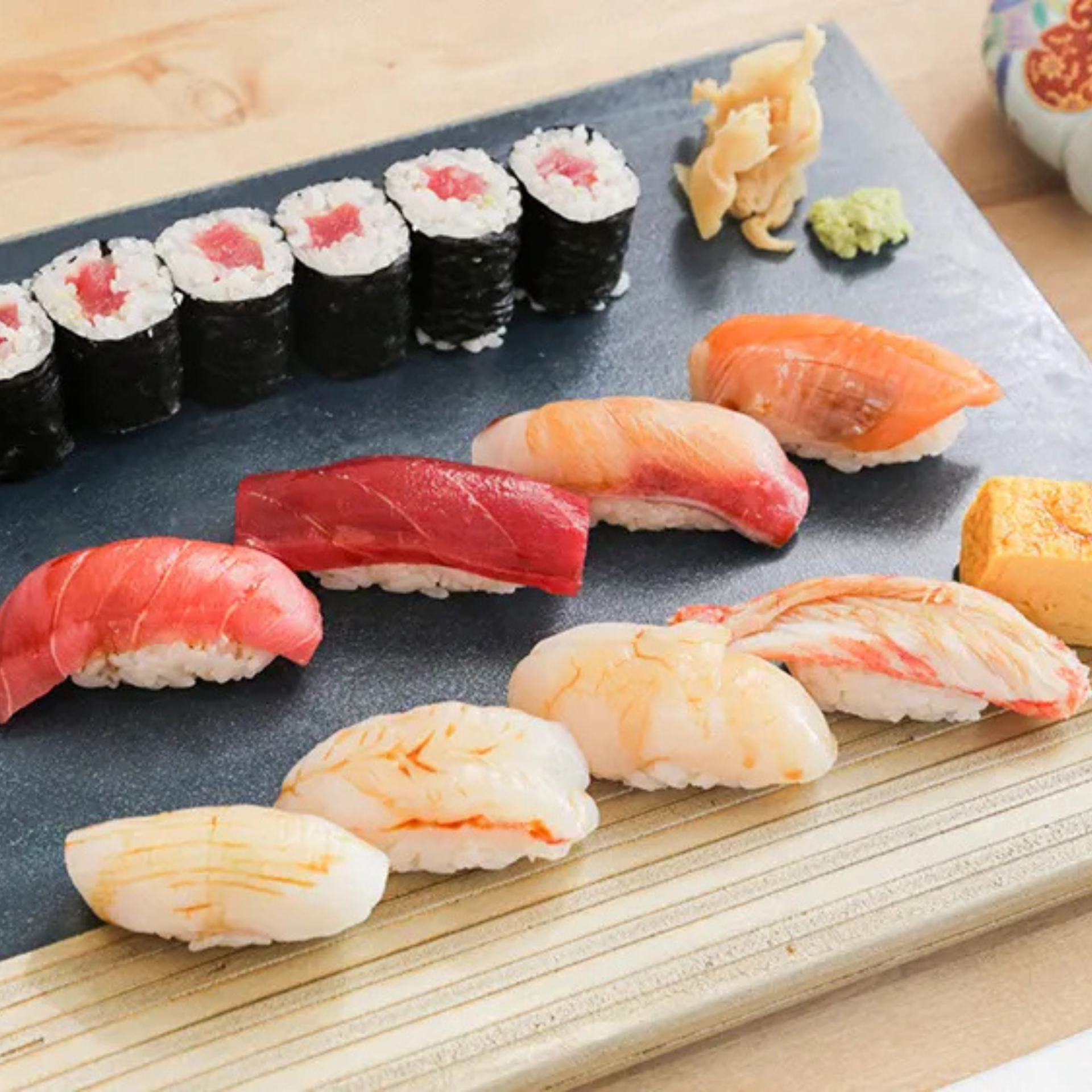 Assorted sushi platter with tuna maki rolls, salmon and tuna nigiri, tamago, shrimp, and wasabi on a dark serving plate