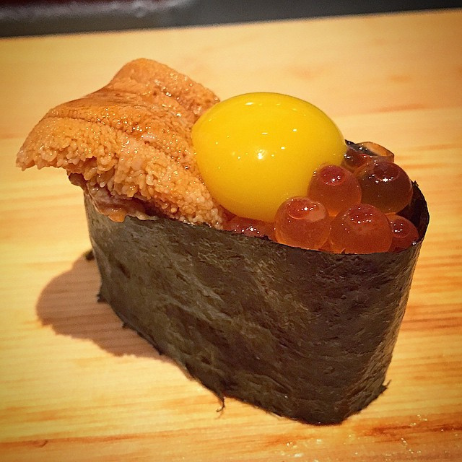 Luxury sushi with uni, quail egg yolk, and salmon roe on nori-wrapped rice