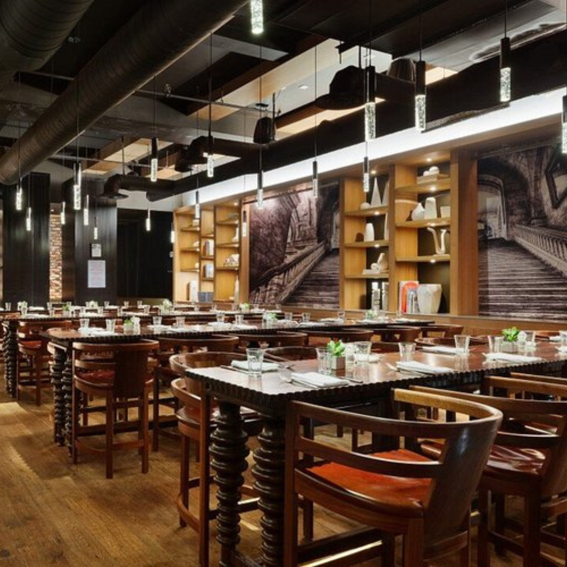 Best Hotel Bars in NYC: Contemporary restaurant with wooden tables, pendant lights, and black-and-white staircase murals on the walls