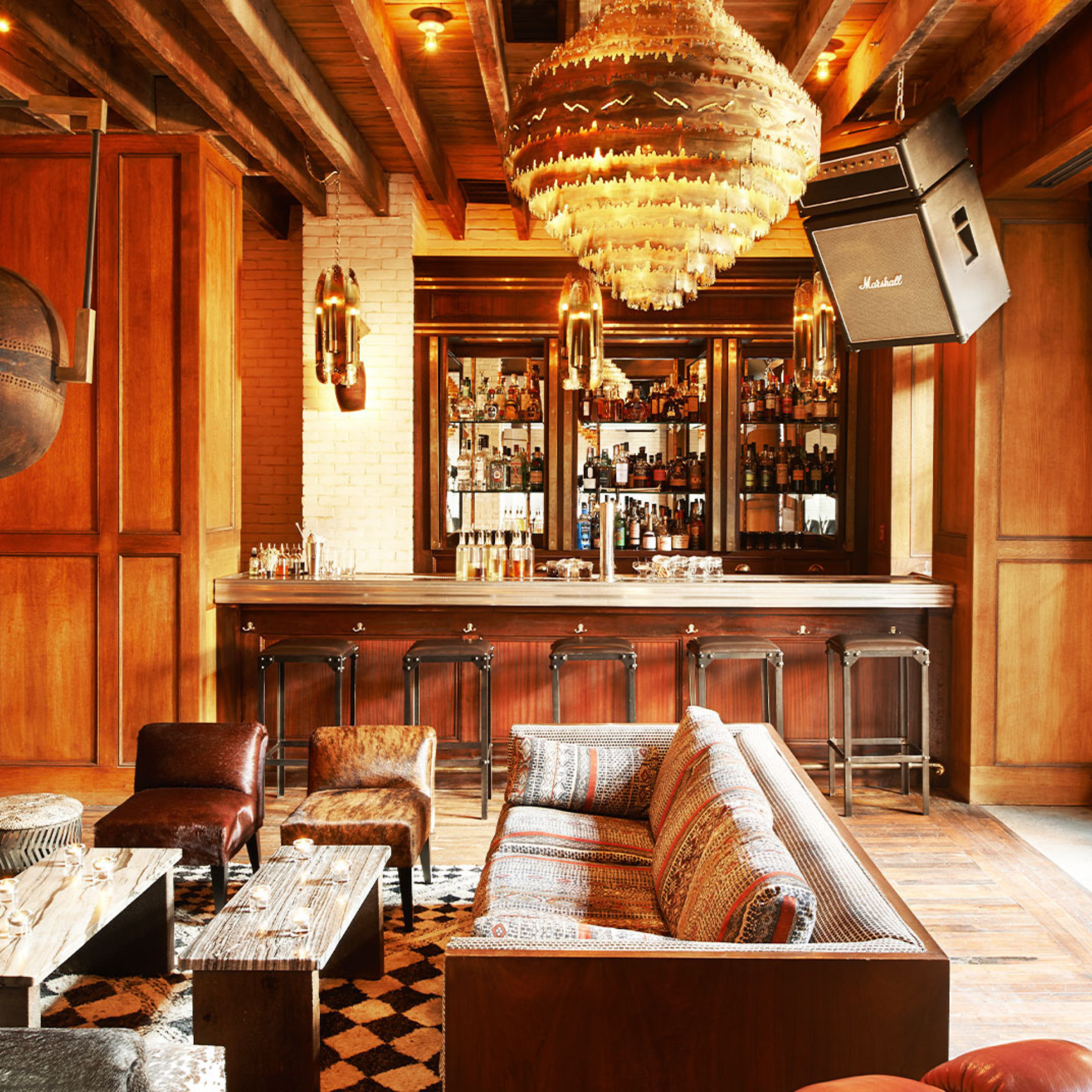 Rustic bar with wooden counter, ornate chandelier, patterned seating, and warm ambient lighting