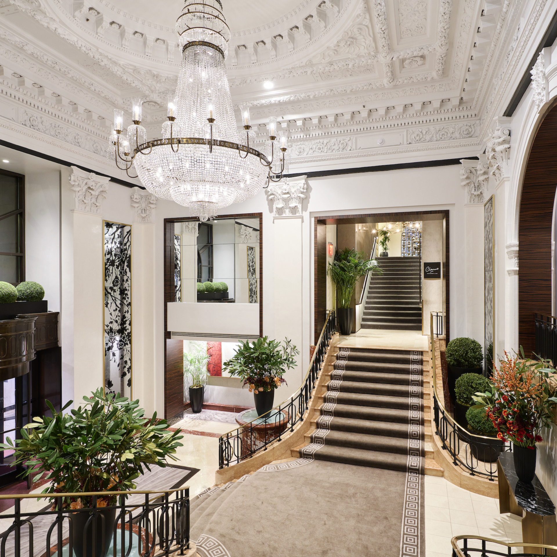 Grand hotel lobby with ornate chandelier, sweeping staircase, and classical decor