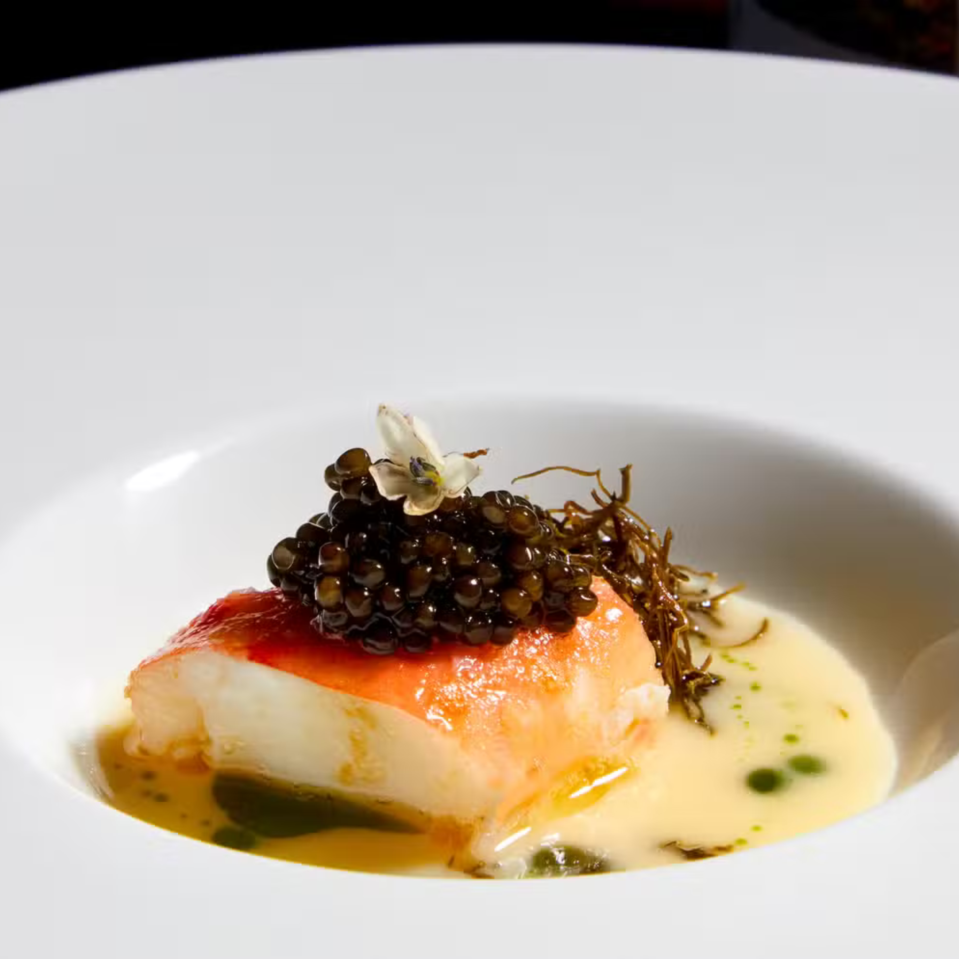 Fine dining dish with seared fish, creamy sauce, black caviar, and edible flower garnish.