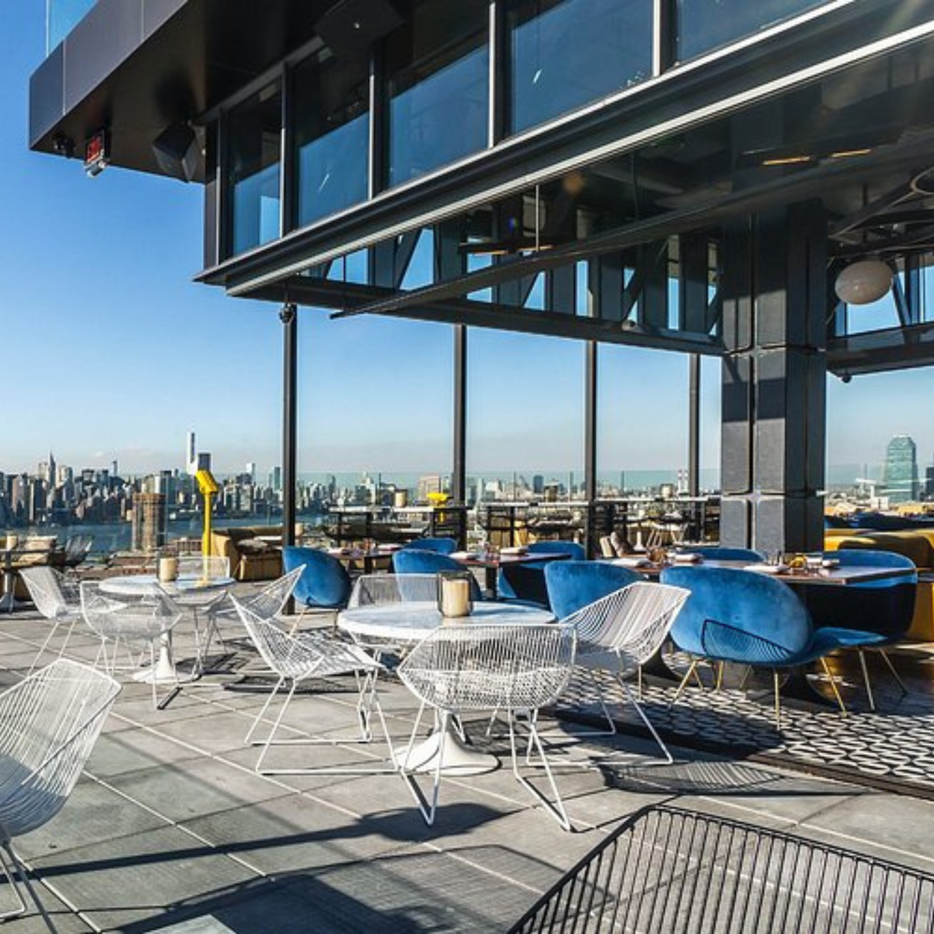 Modern rooftop lounge with velvet chairs, wireframe seating, and panoramic city skyline views
