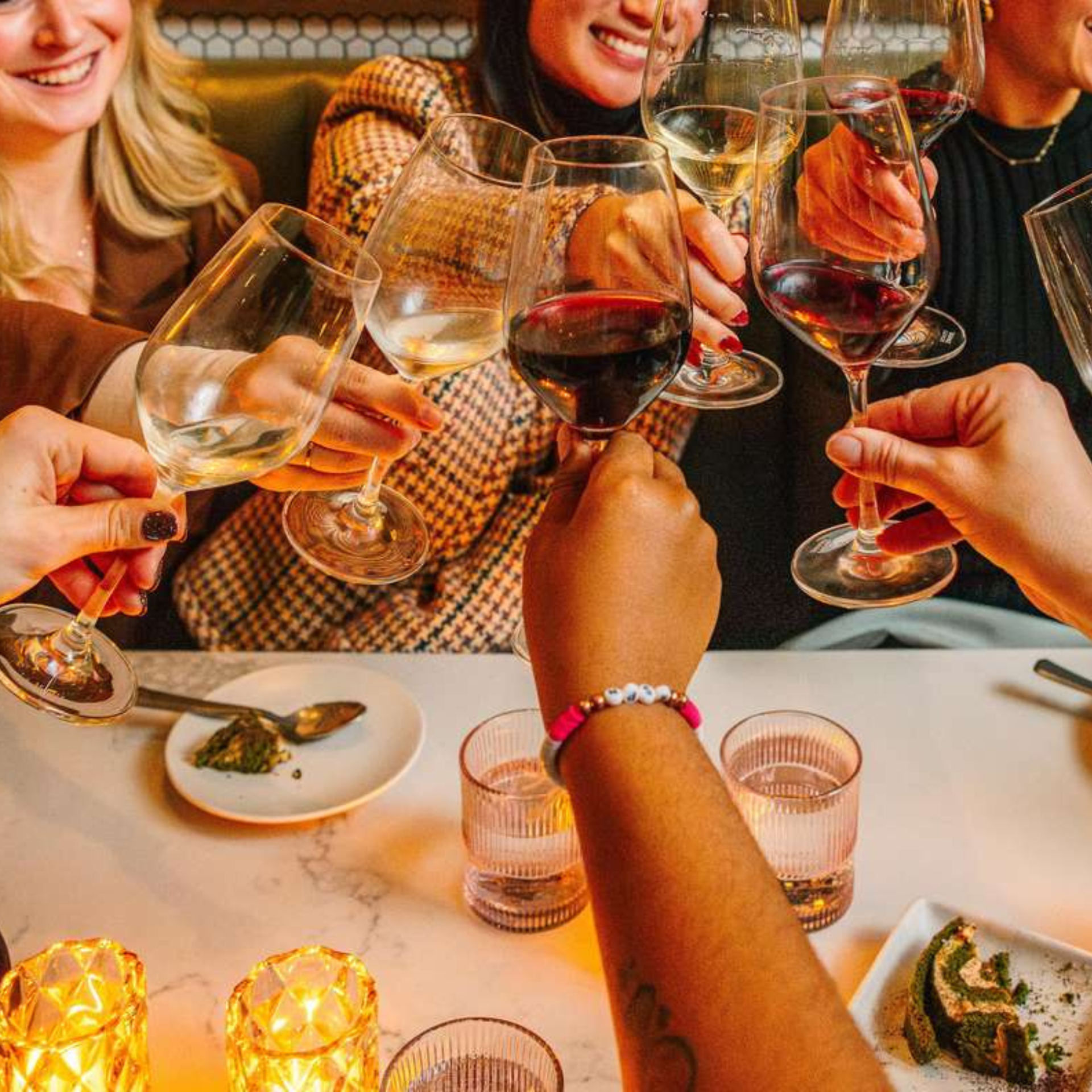 Group of friends raising wine glasses in a cozy restaurant with candles and food on the table