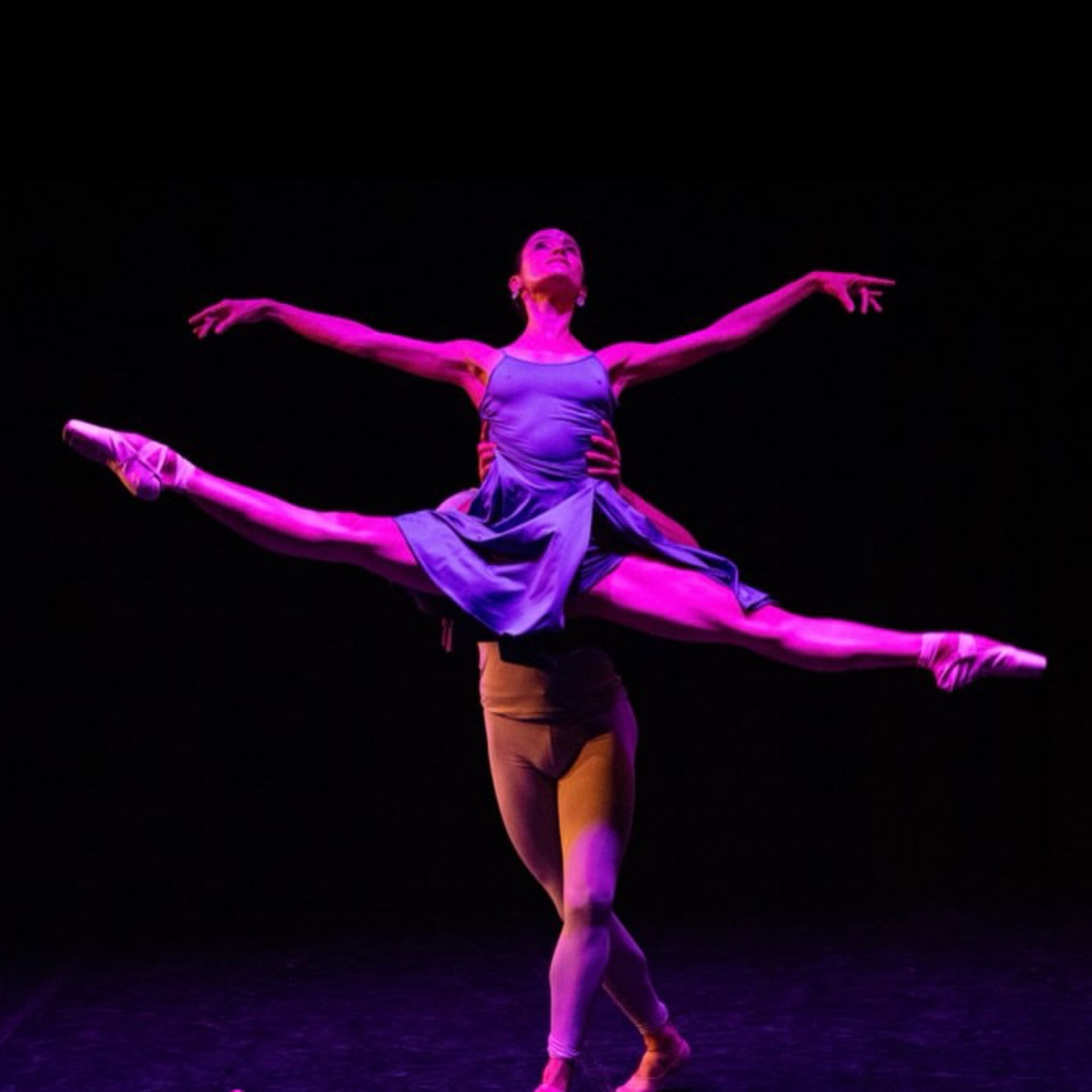Two ballet dancers perform a dramatic leap under pink and purple stage lighting