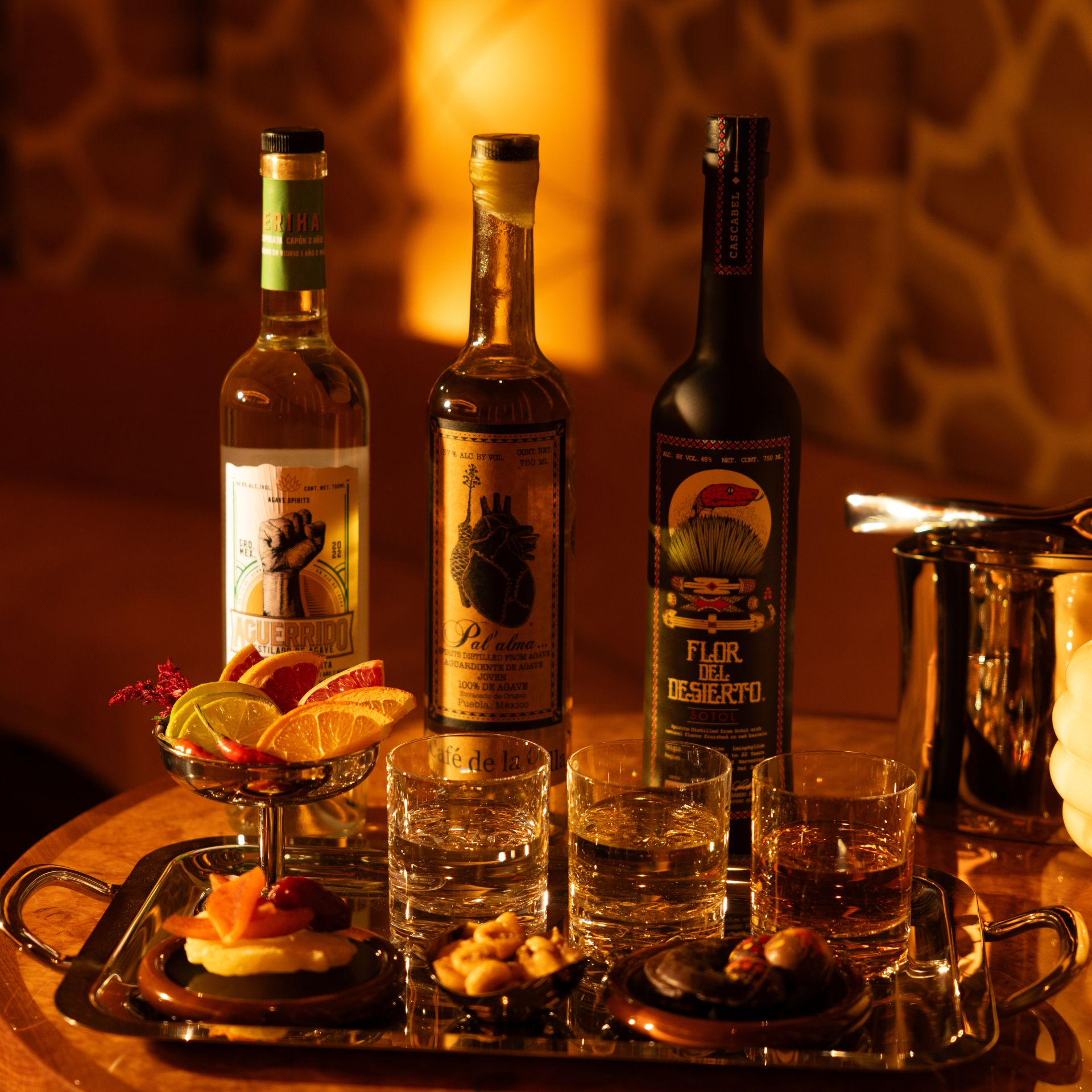 Tabletop display with mezcal bottles, glasses, and garnishes under warm lighting